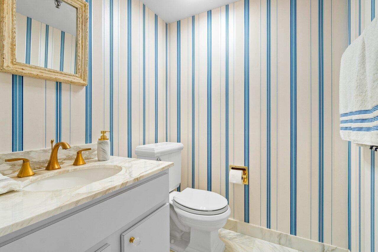 Bathroom with blue-striped wallpaper, marble vanity, and brass fixtures