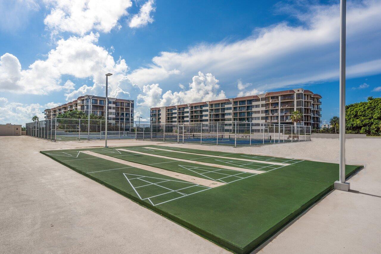 Outdoor shuffleboard courts with fenced tennis courts and condominium buildings behind them.