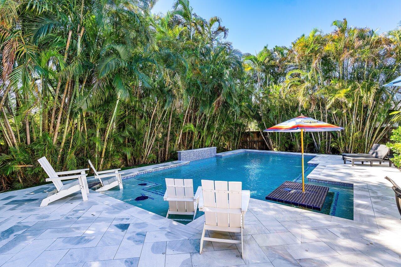 Outdoor pool surrounded by dense palms, with white Adirondack chairs and a striped umbrella.