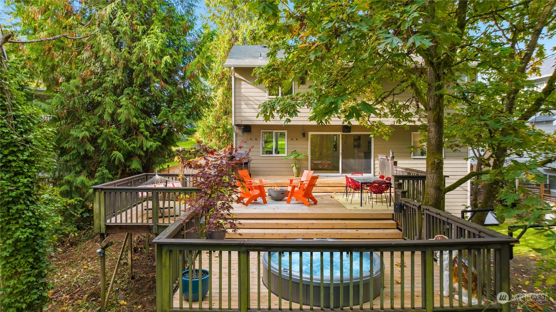 Home’s wooded backyard deck with a hot tub, orange lounge chairs, and outdoor dining area.