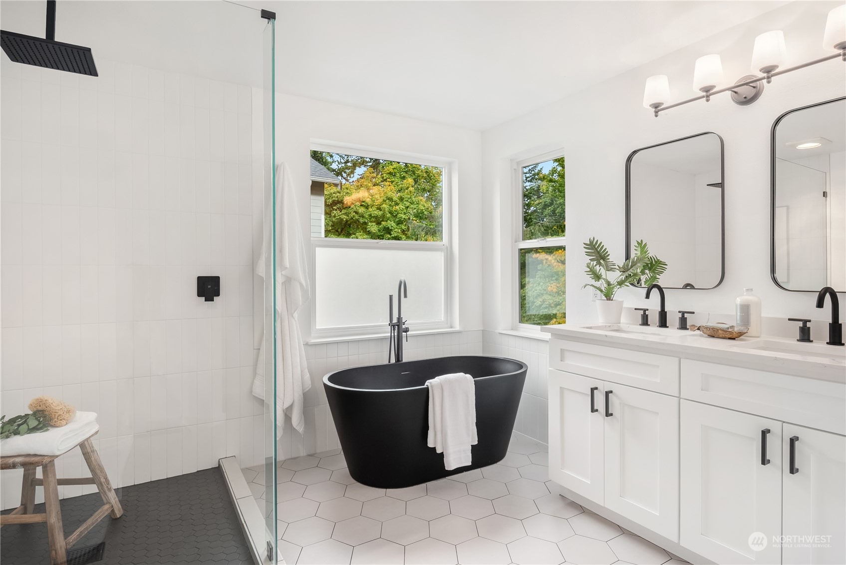 Bathroom with a black freestanding tub, glass shower, and white double vanity beneath two windows.