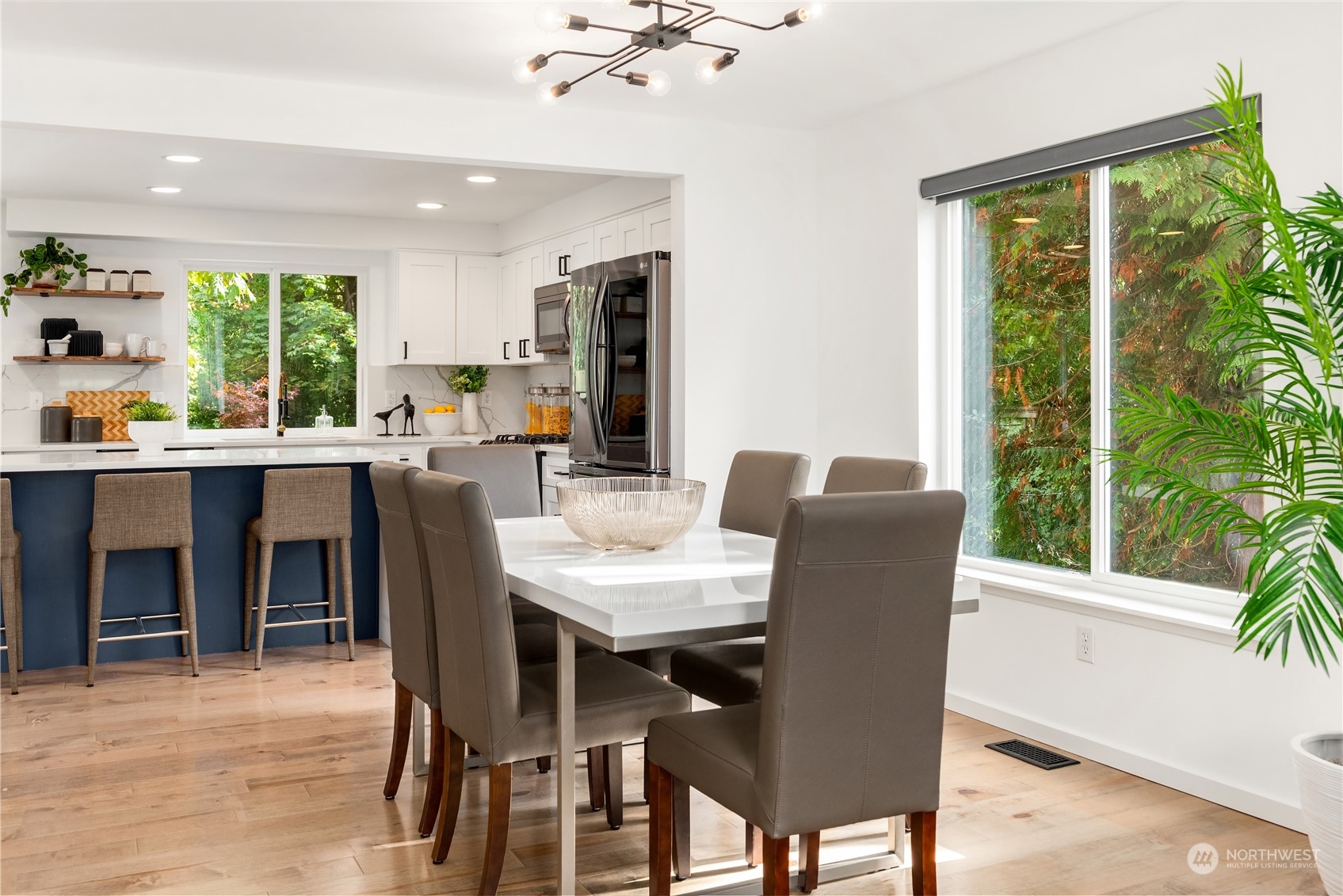 Open-plan kitchen and dining area with a navy island, white cabinetry, and large windows overlooking greenery.