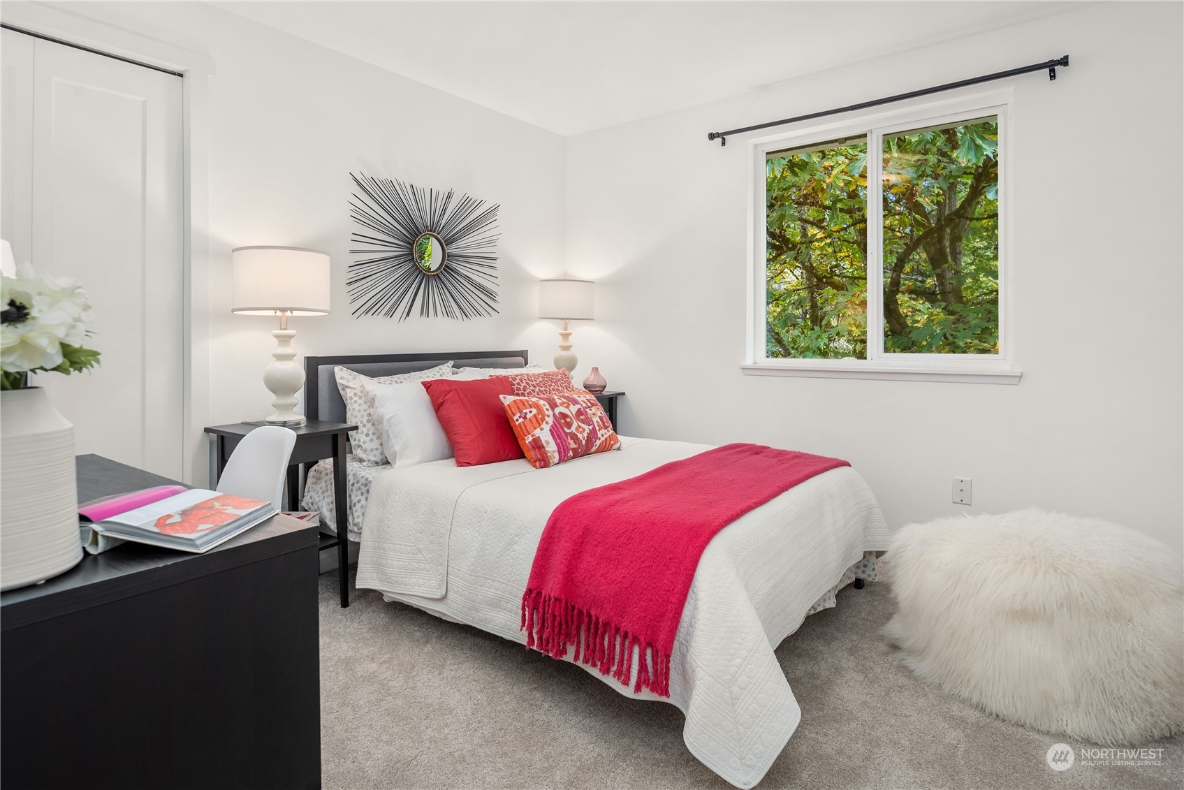 Bedroom with white bedding, a vivid pink throw, and a large window overlooking leafy trees.