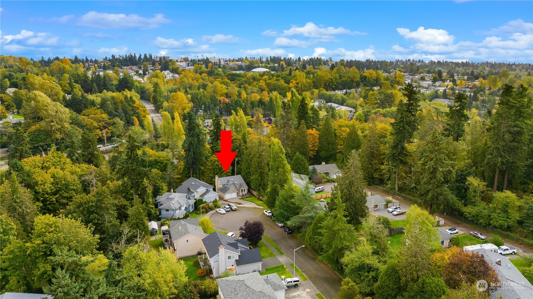 Aerial view of the home marked by a red arrow, surrounded by autumn trees and neighboring houses.