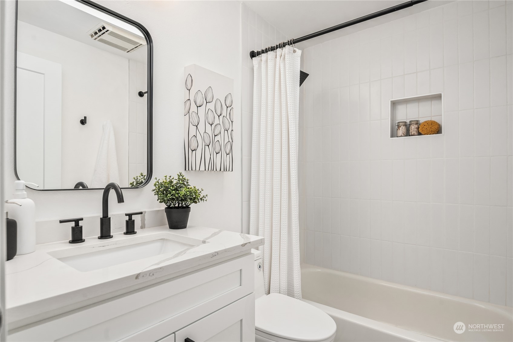Bright bathroom with a veined white vanity, black fixtures, and a tiled tub and shower.