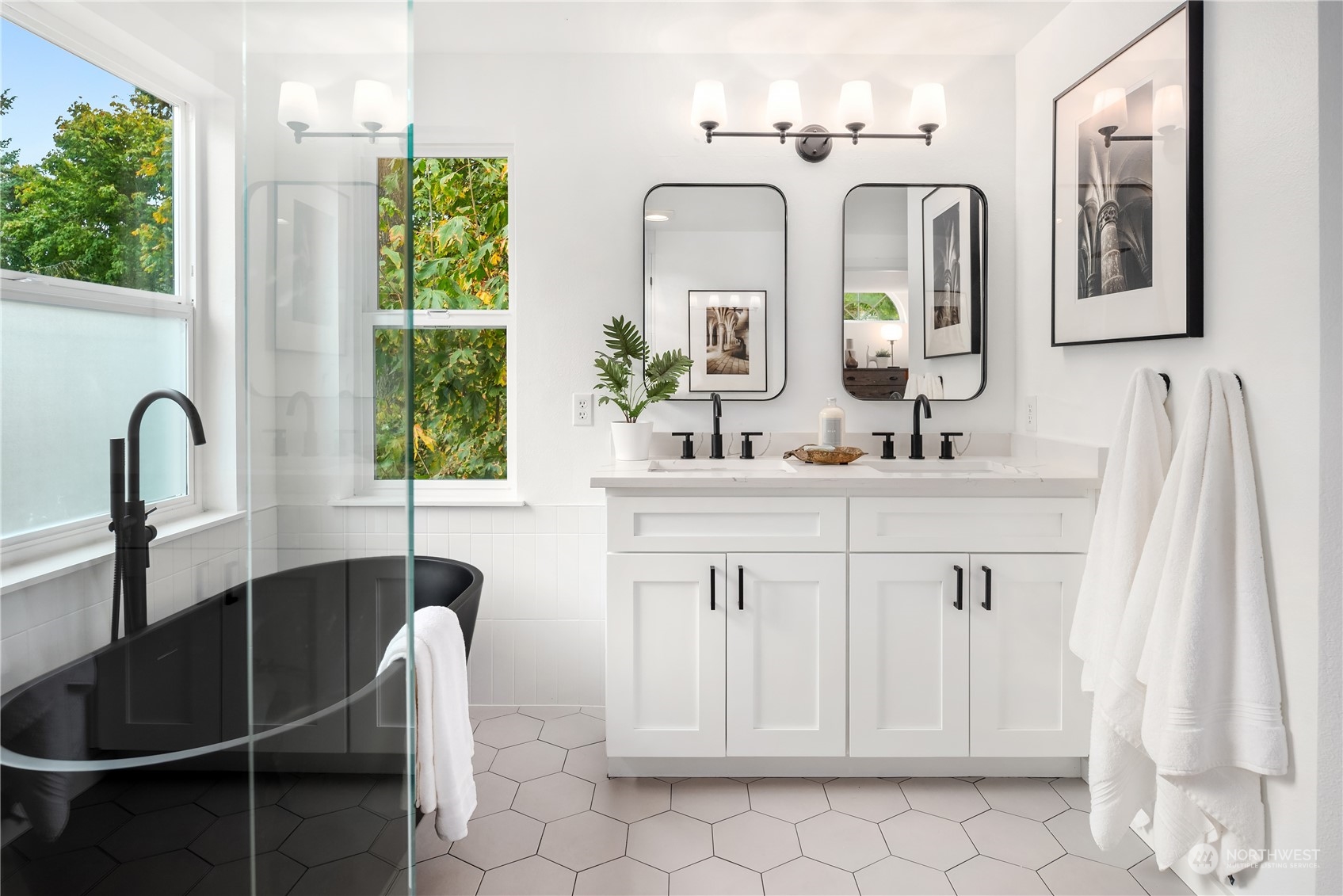 Bathroom with a black freestanding tub, white double vanity, and large windows.