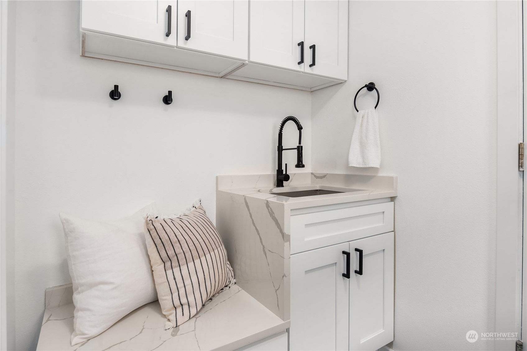 Laundry room with white cabinets, a stone sink, black faucet, and built-in bench with pillows.