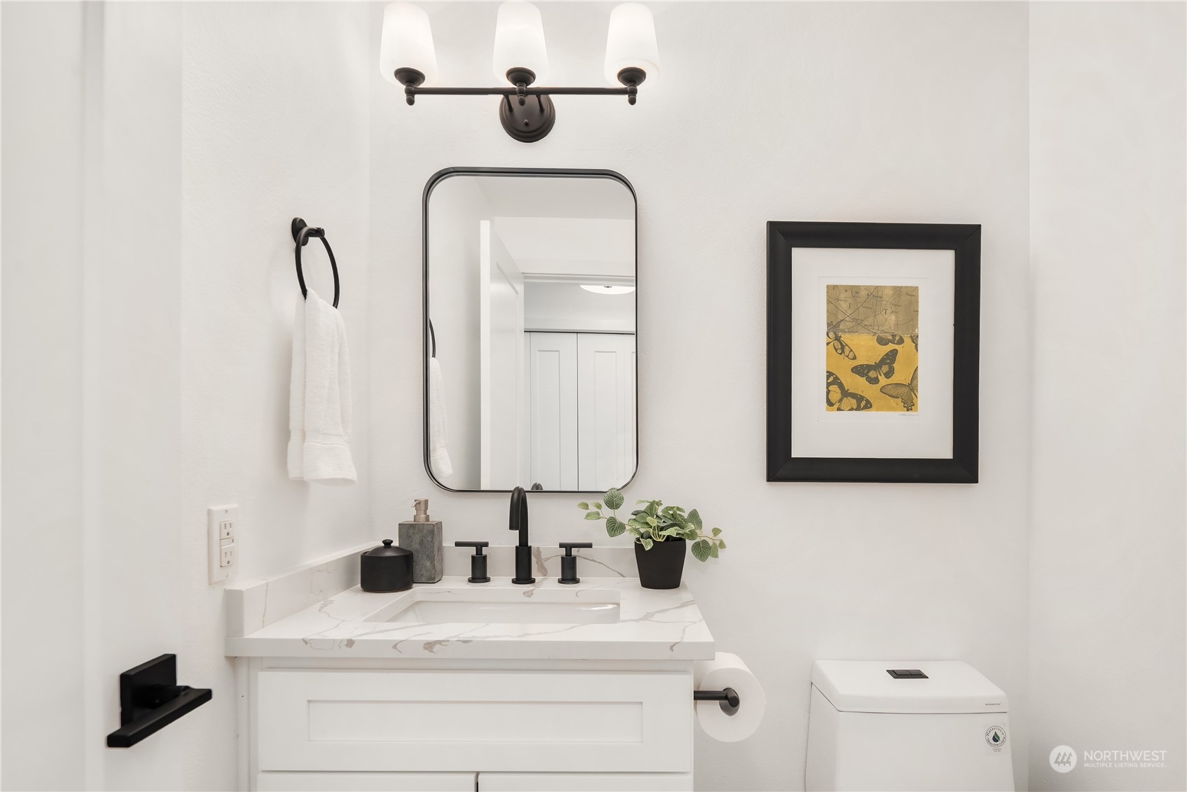 Bathroom vanity with veined countertop, matte-black fixtures, rounded mirror, and framed butterfly artwork.