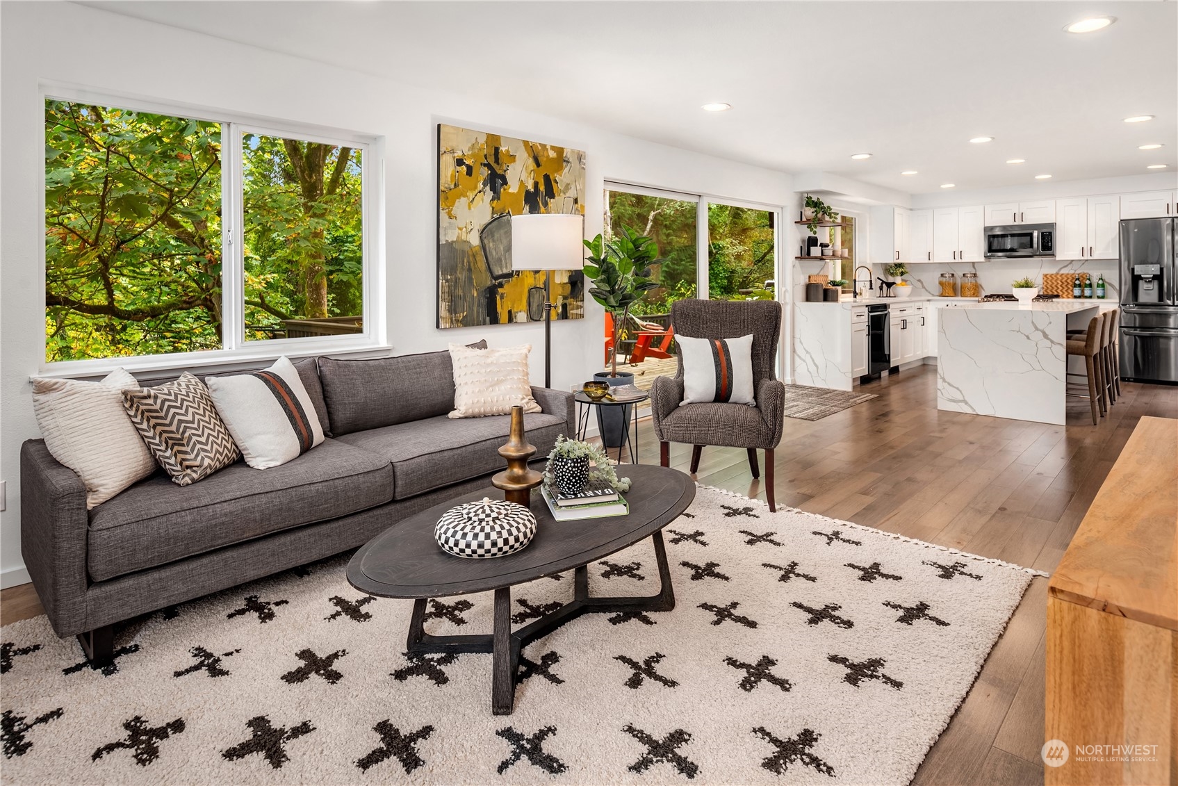 Open-plan living room and kitchen with a gray sofa, white cabinetry, and a marble-look island.