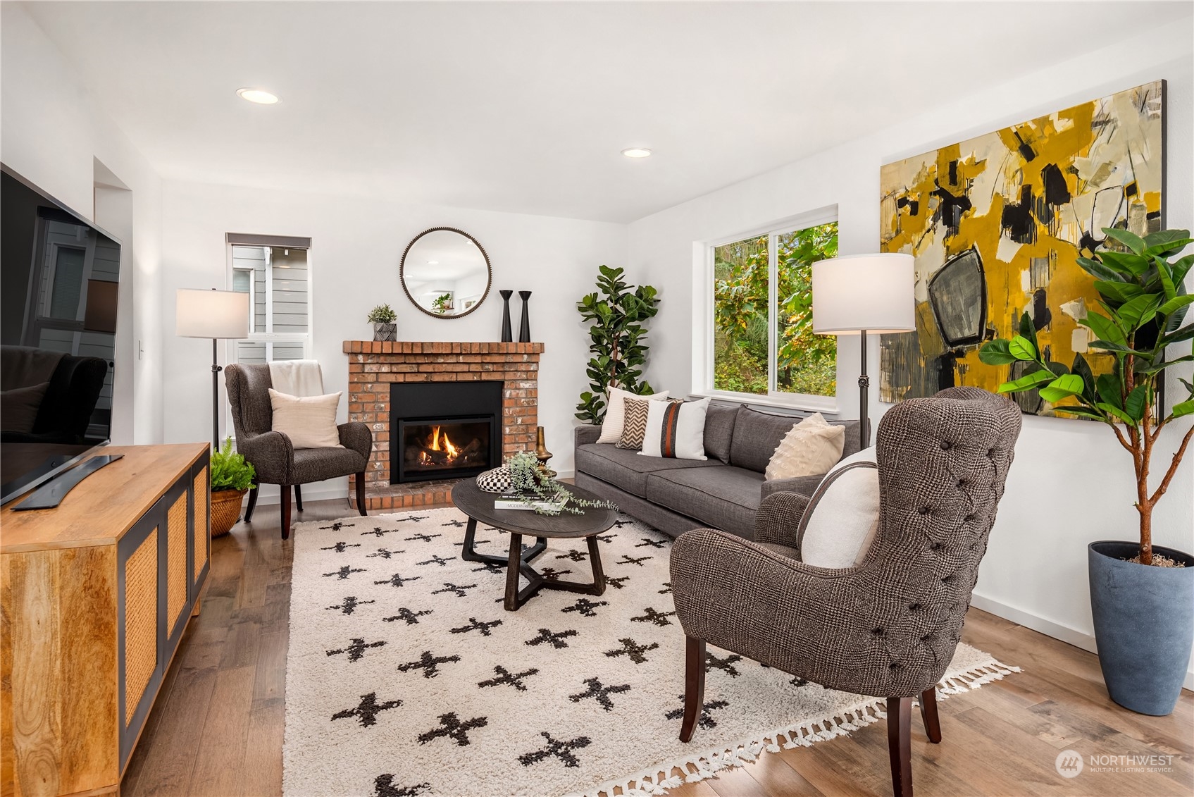 Staged living room with a brick fireplace, gray sofa, and large yellow-and-black abstract painting.