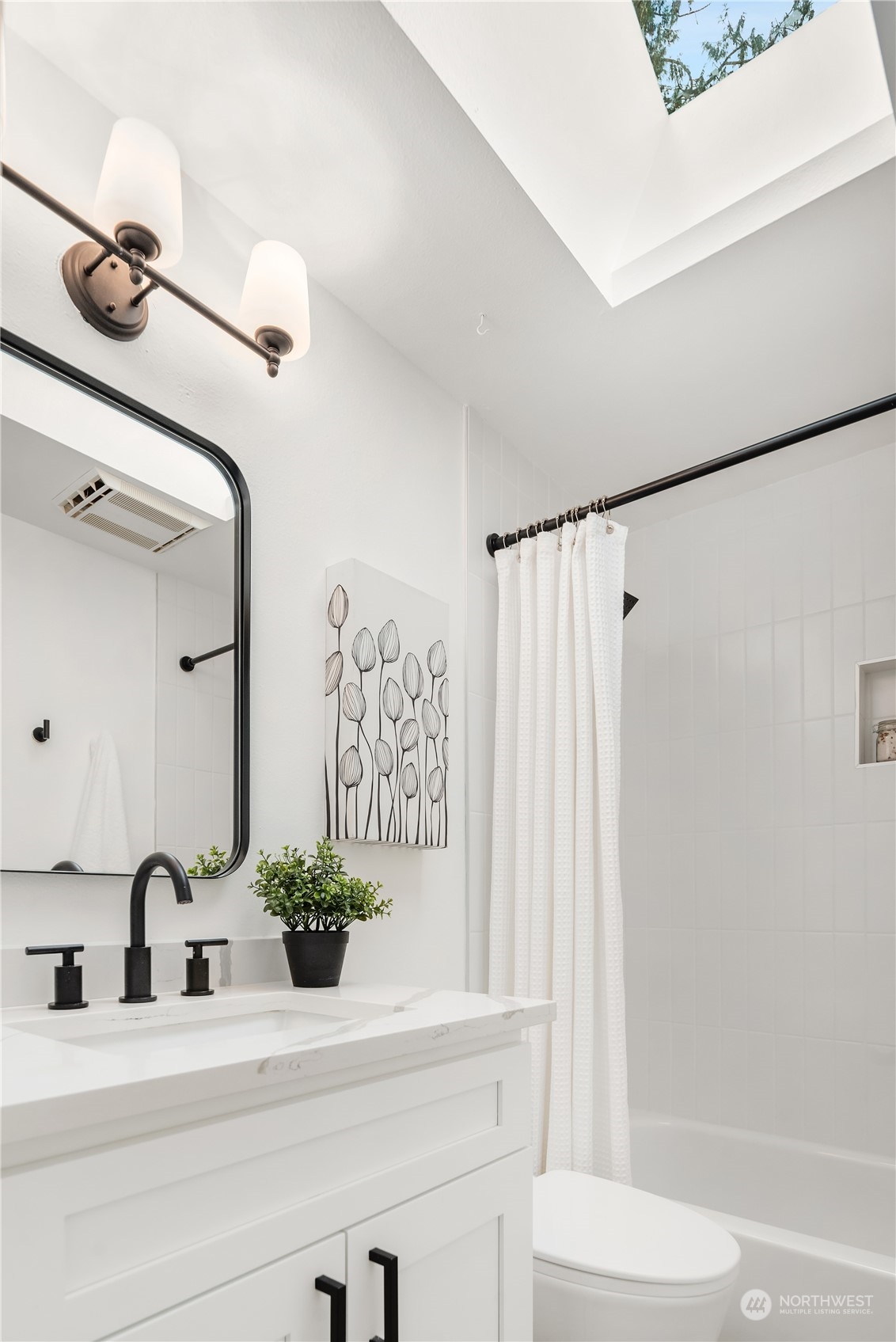 Bathroom with a white vanity, black fixtures, a curtained tub-shower, and a skylight.