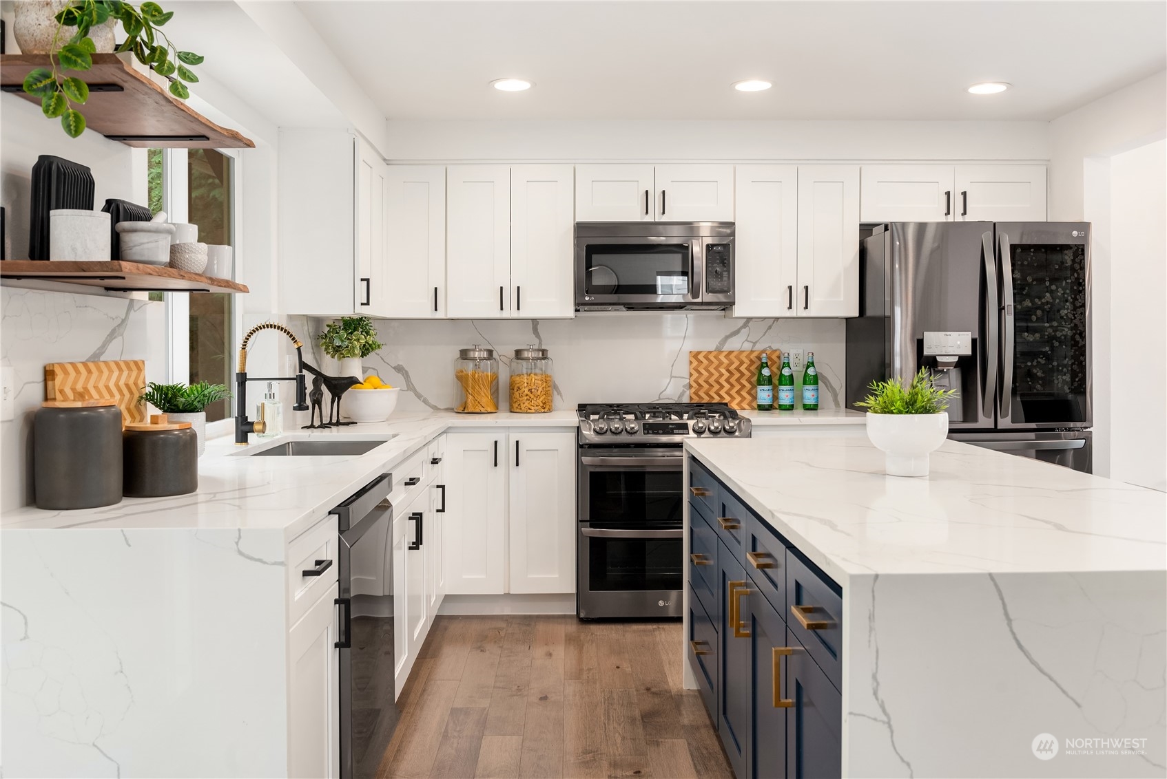 Modern kitchen with a navy island, marble-look counters, white cabinets, and stainless steel appliances.