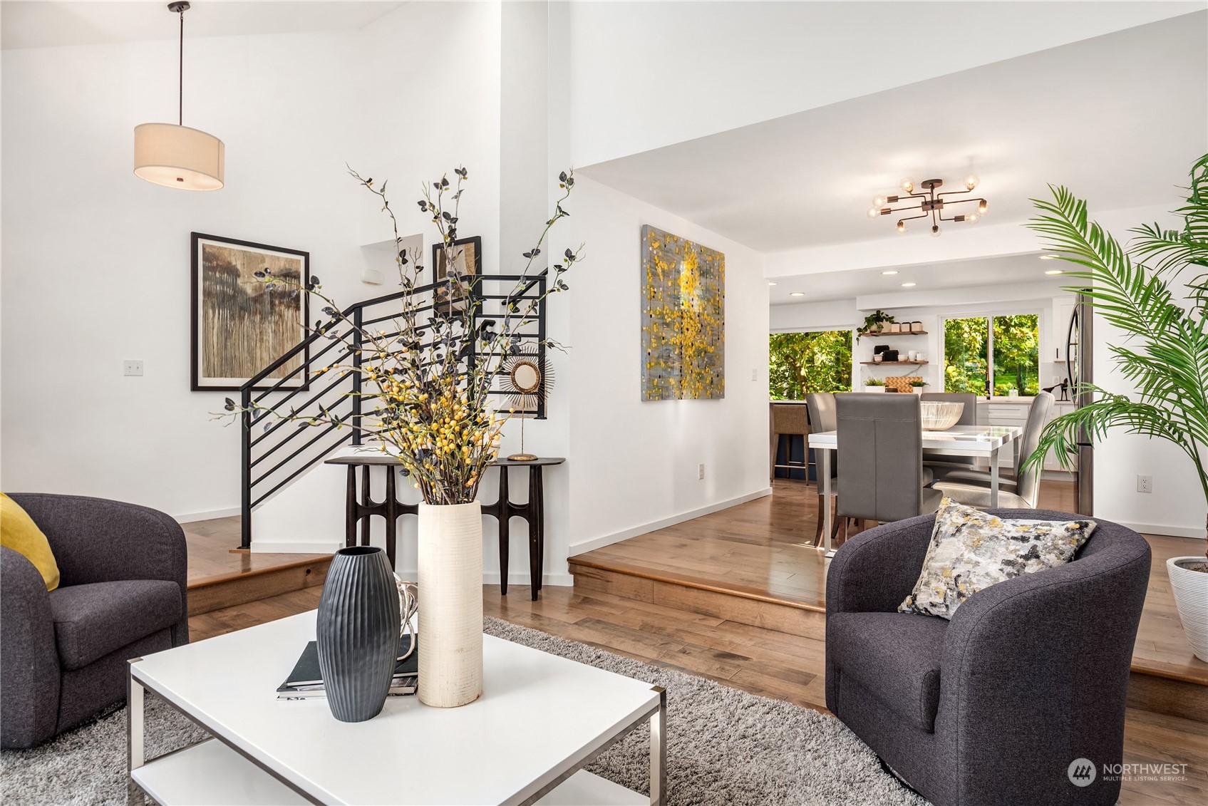 Staged living room with a black metal staircase and an open view into the dining area and kitchen.