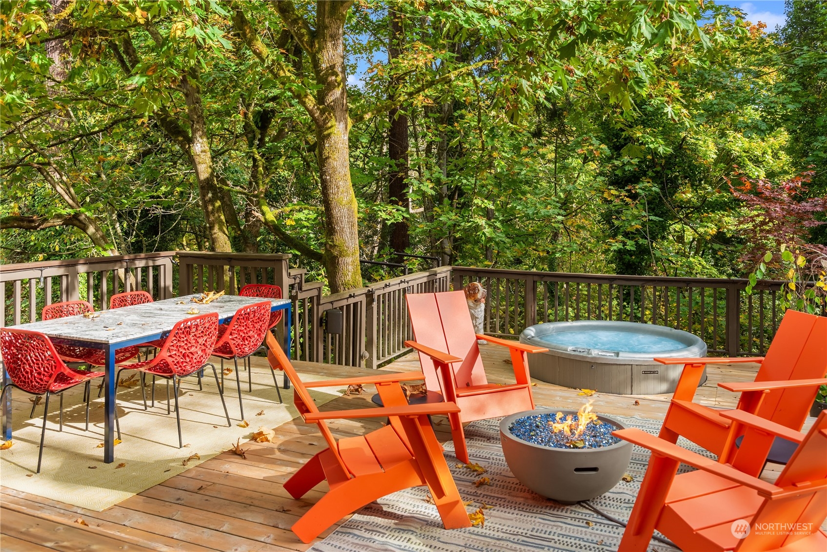 Wooded deck with orange lounge chairs, a hot tub, fire pit, and outdoor dining table.