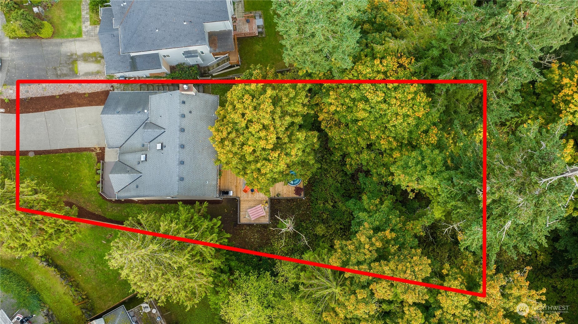 Aerial view of a wooded property outlined in red, with a gray-roofed house and deck.