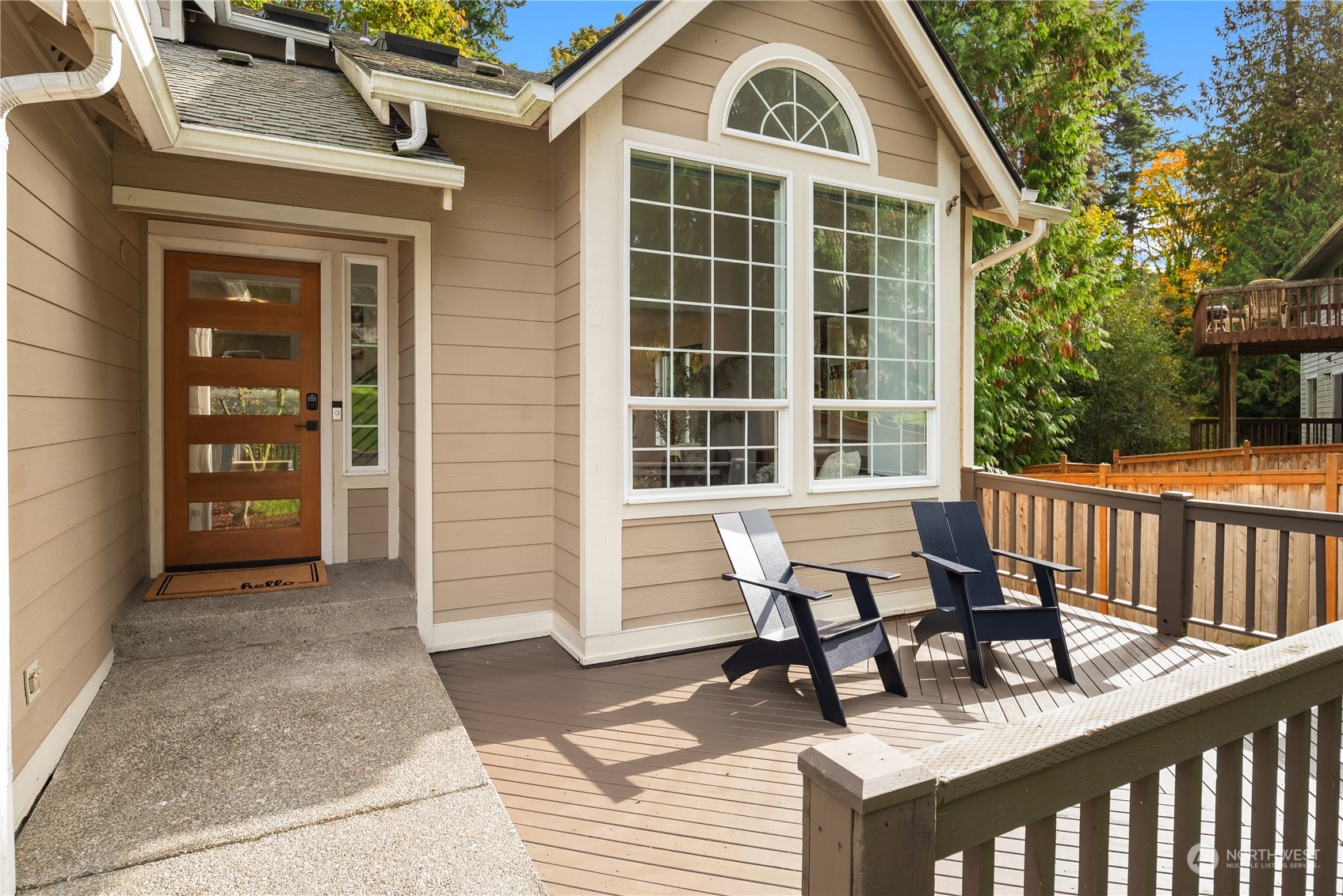 House entrance and wood deck with two Adirondack chairs beside large grid windows.