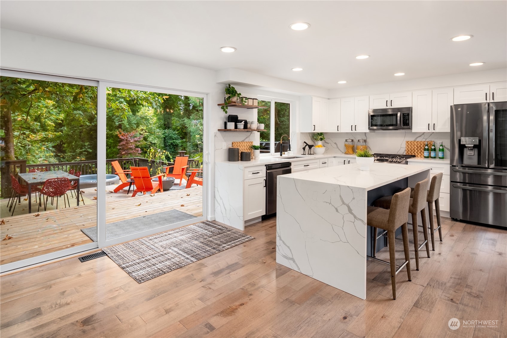 Bright white kitchen with a large marble-look island opening onto a wooded deck.