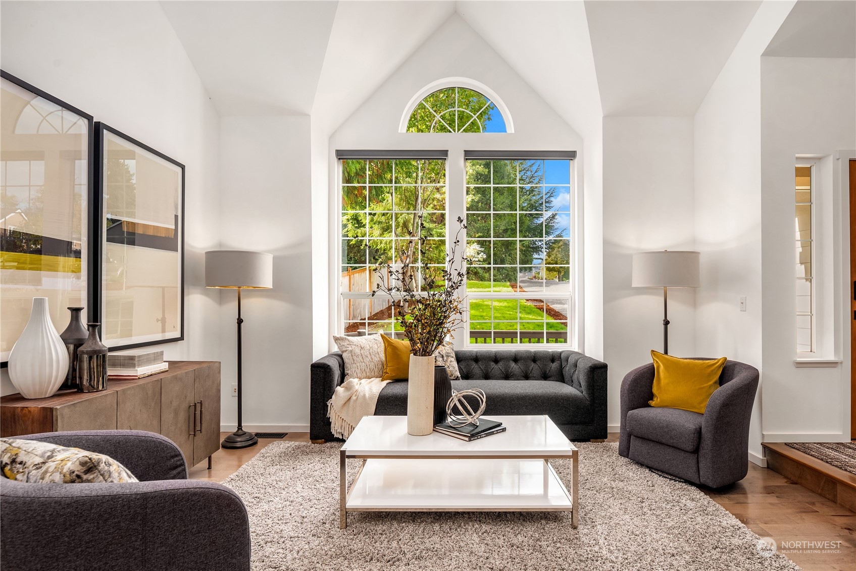 Staged living room with vaulted ceiling, arched windows, and gray seating.