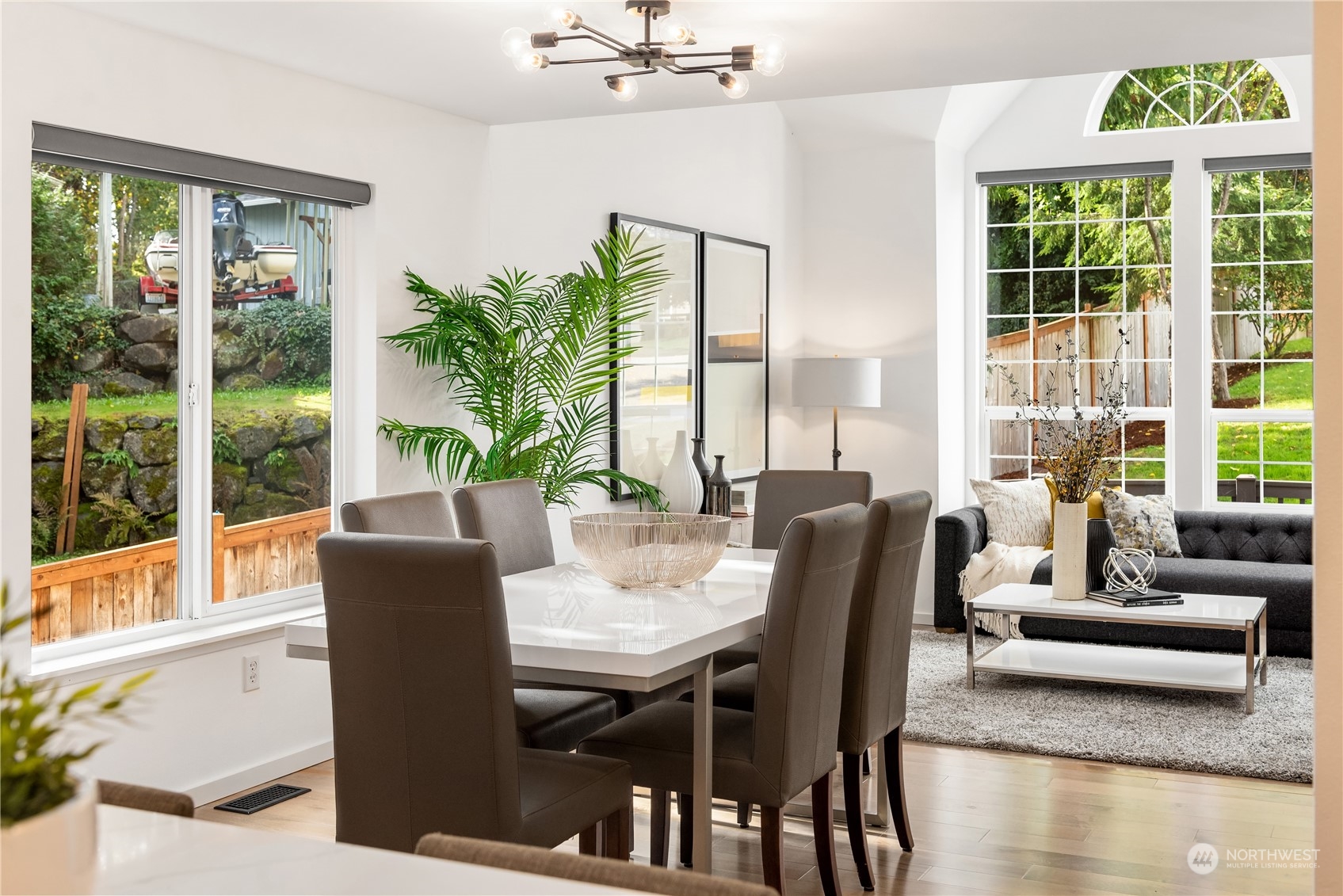 Dining room with a white table and brown chairs beside a living area with large windows.