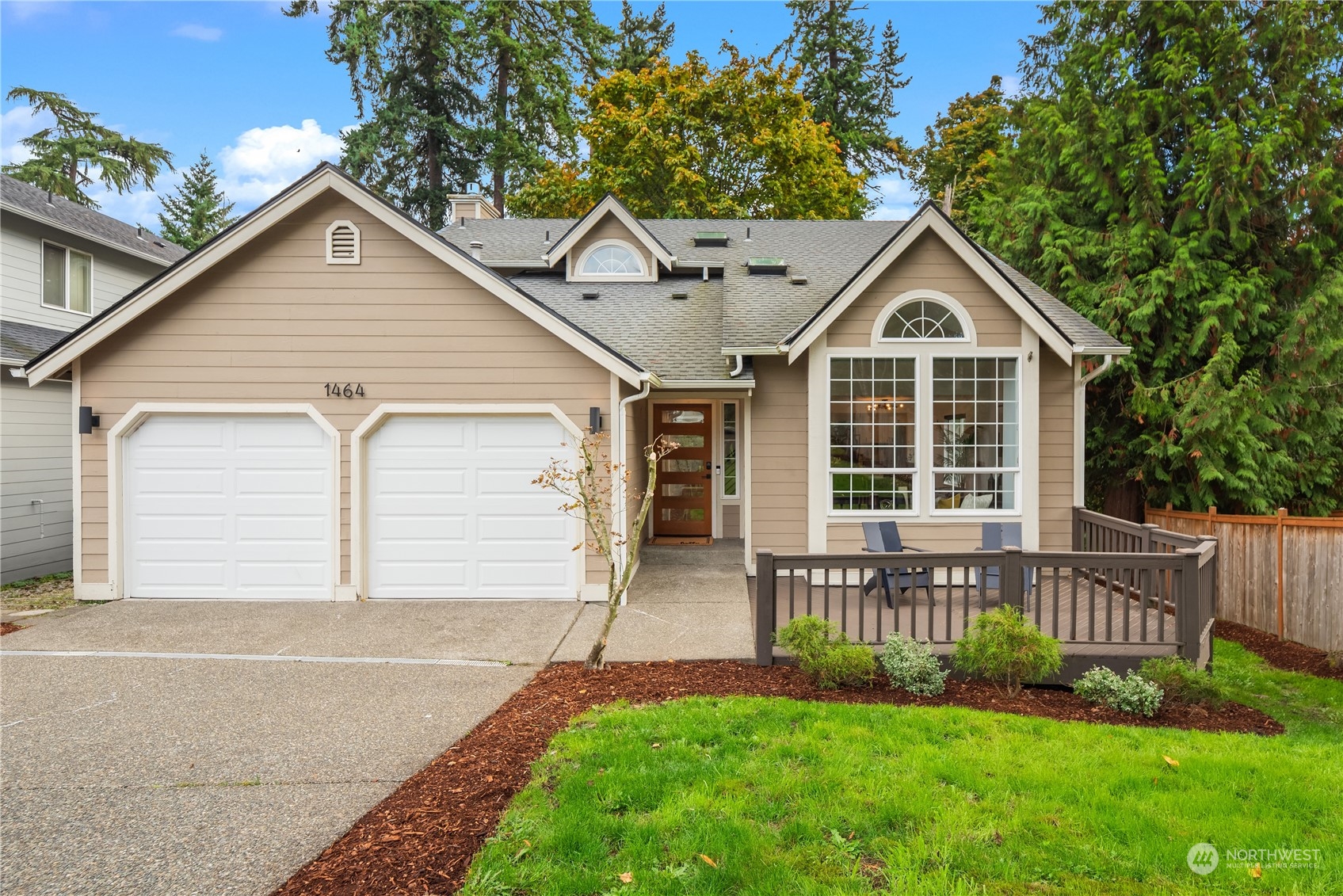 Tan house with two garage doors, arched windows, and a fenced deck.