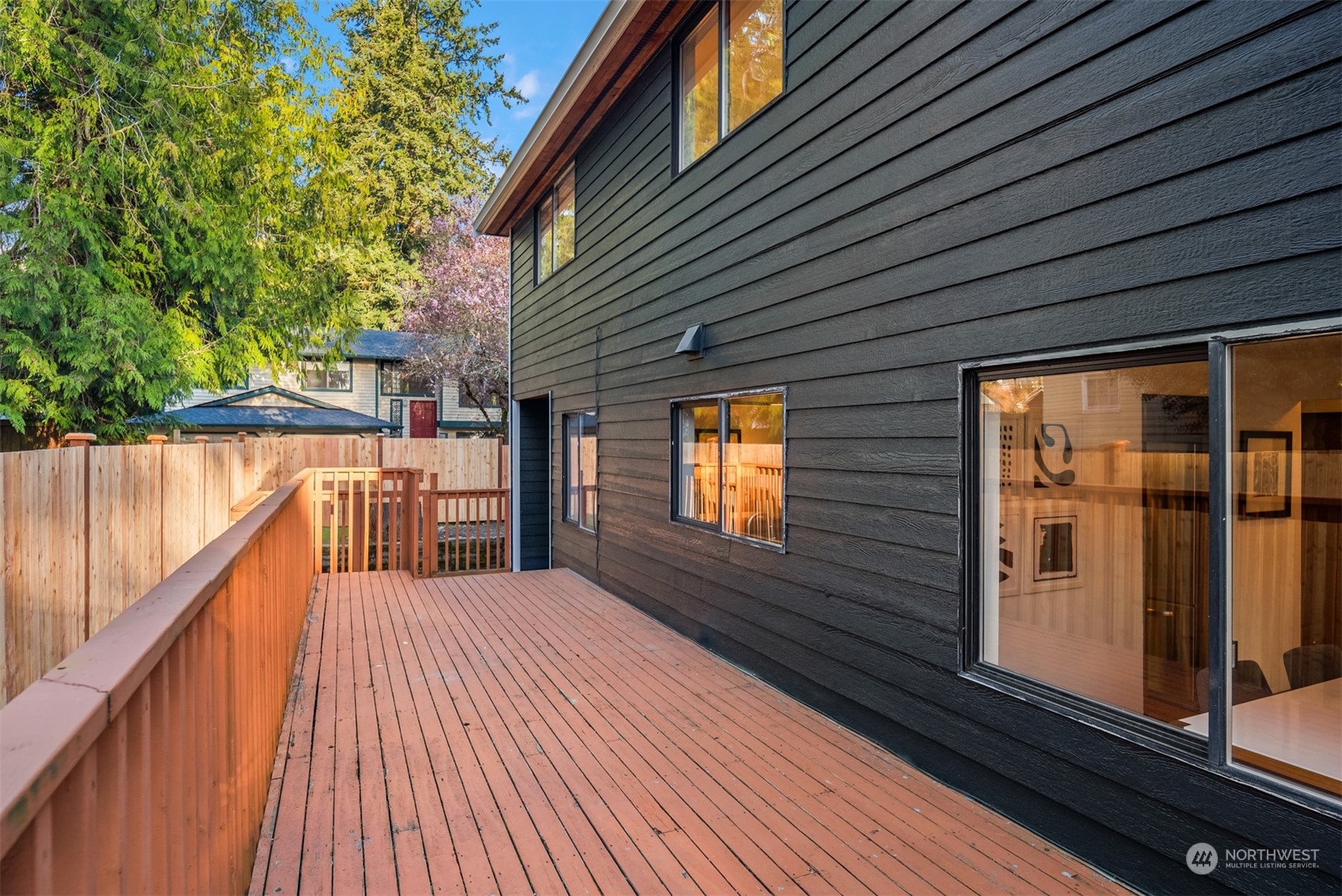 Wood deck along a dark-sided home, with a fenced yard and trees beyond.