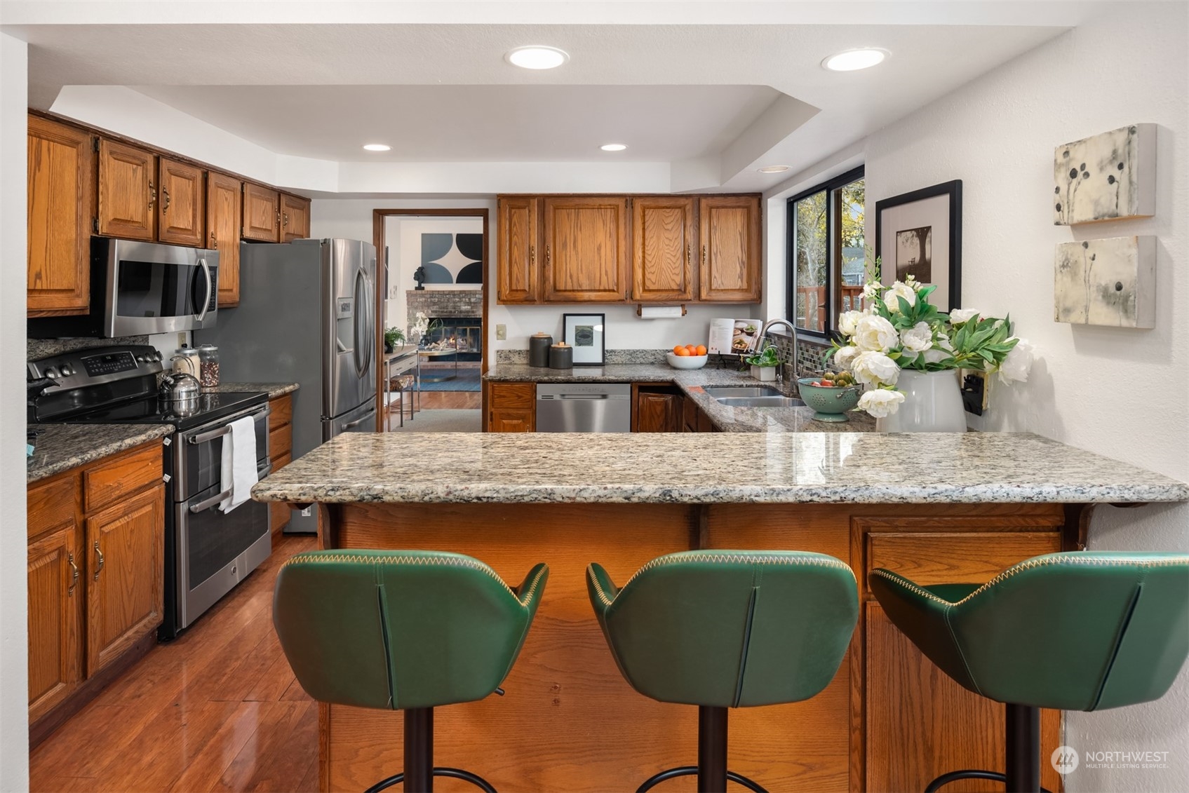 Kitchen with a granite island, green bar stools, wood cabinets, and stainless steel appliances.