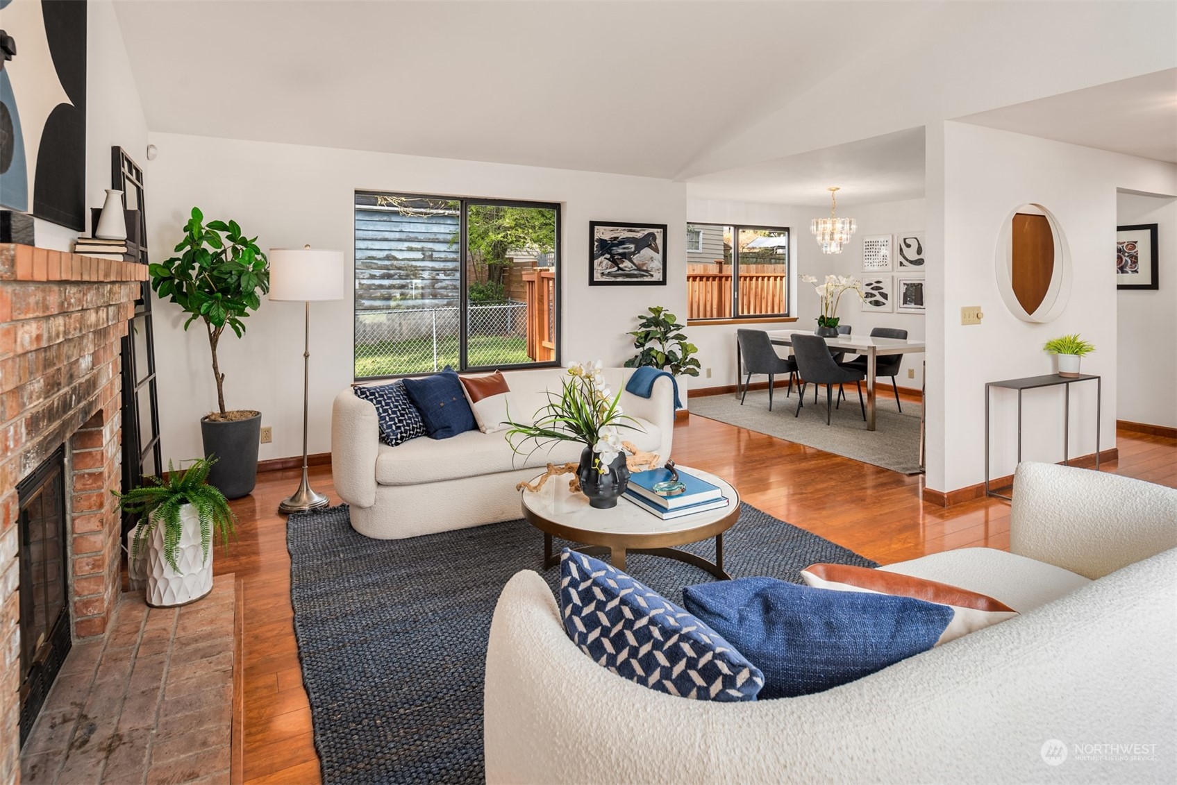 Living room with a brick fireplace, white sofas, and an adjoining dining area.