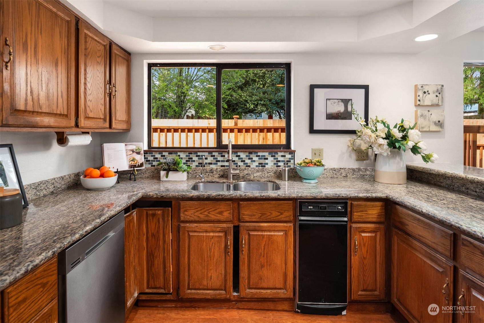 Kitchen with wood cabinets, granite counters, a tiled backsplash, and a window overlooking a wooden deck.