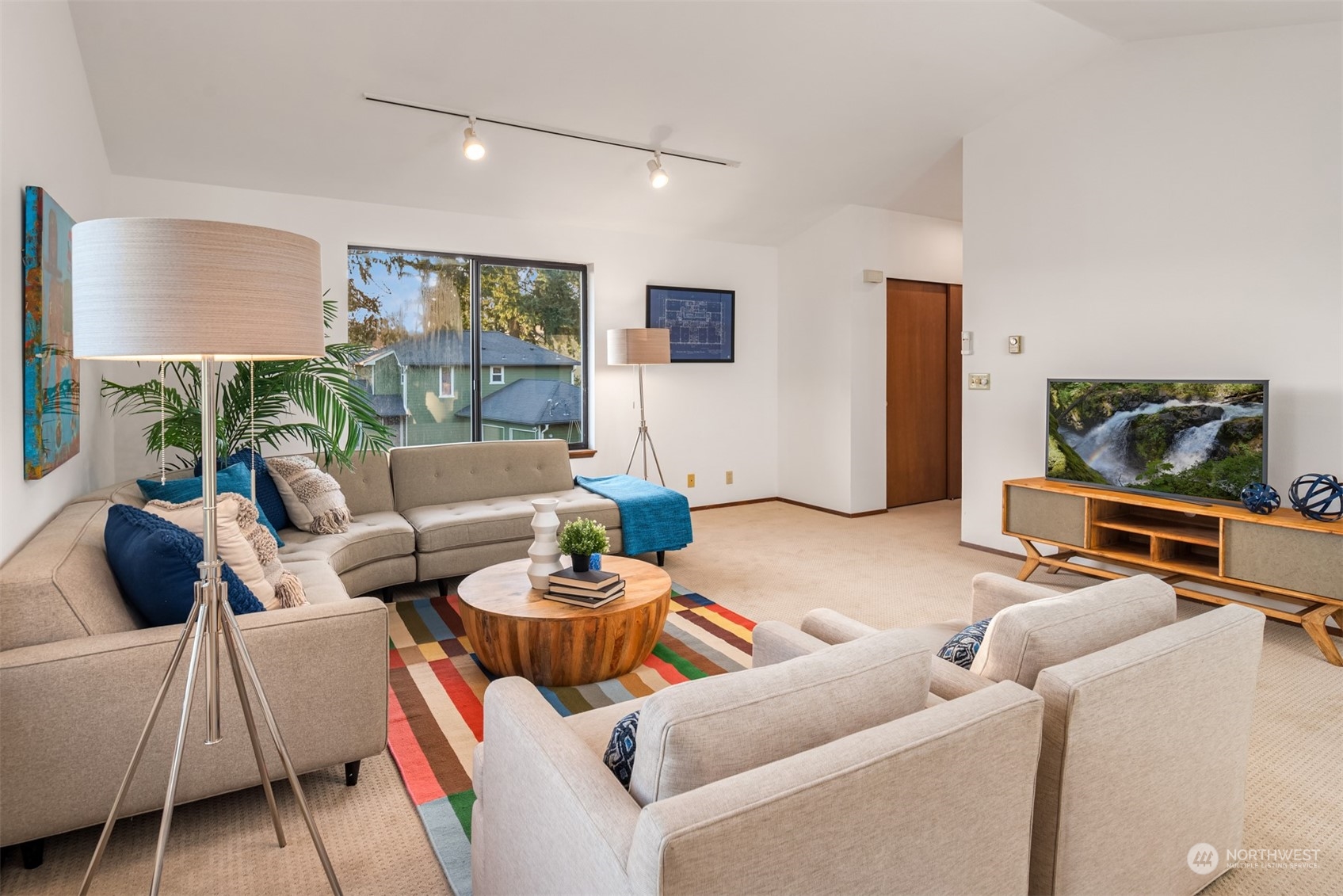 Furnished living room with a beige sectional, colorful rug, and large window.