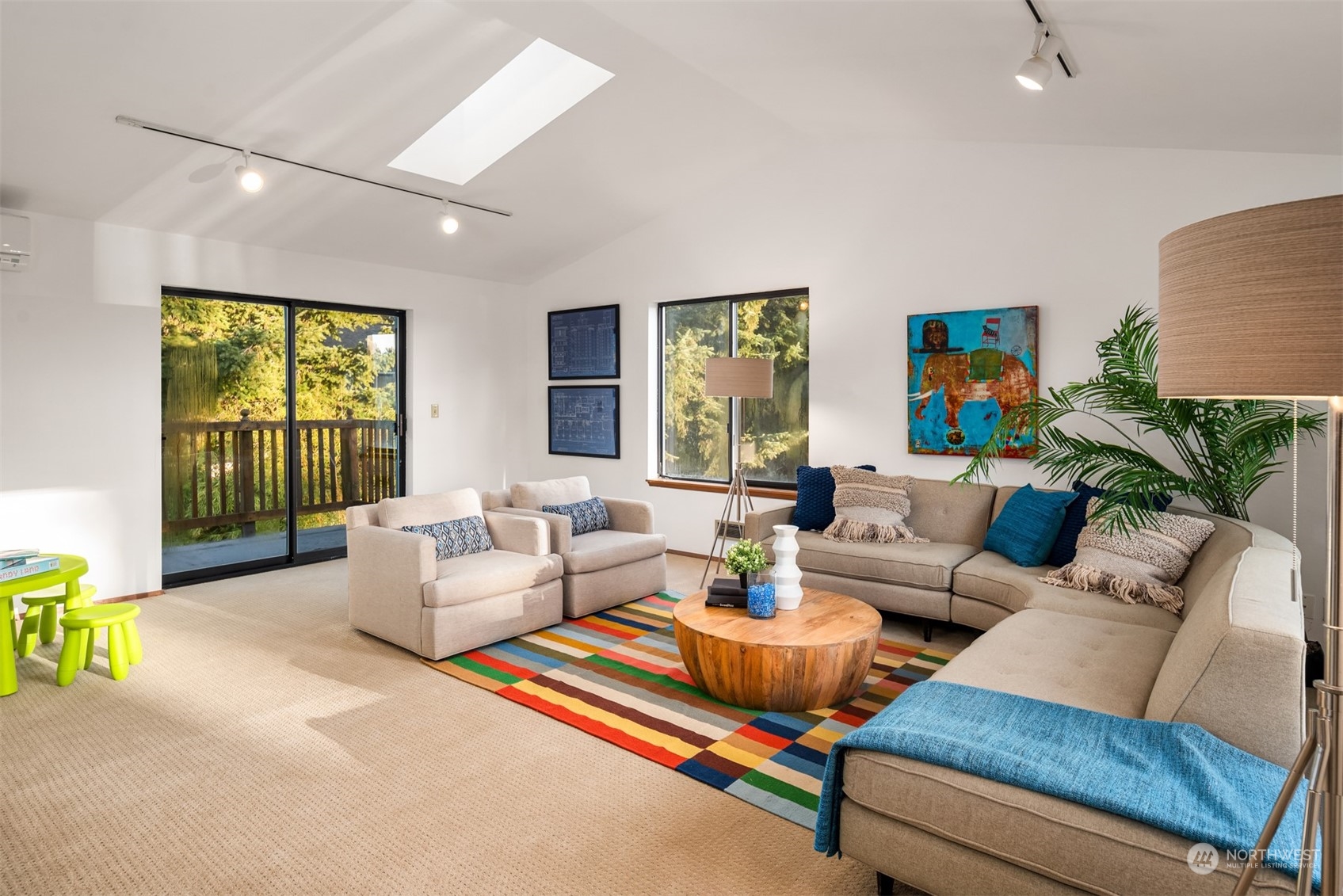 Furnished living room with a skylight, colorful rug, and sliding doors opening onto a leafy deck.