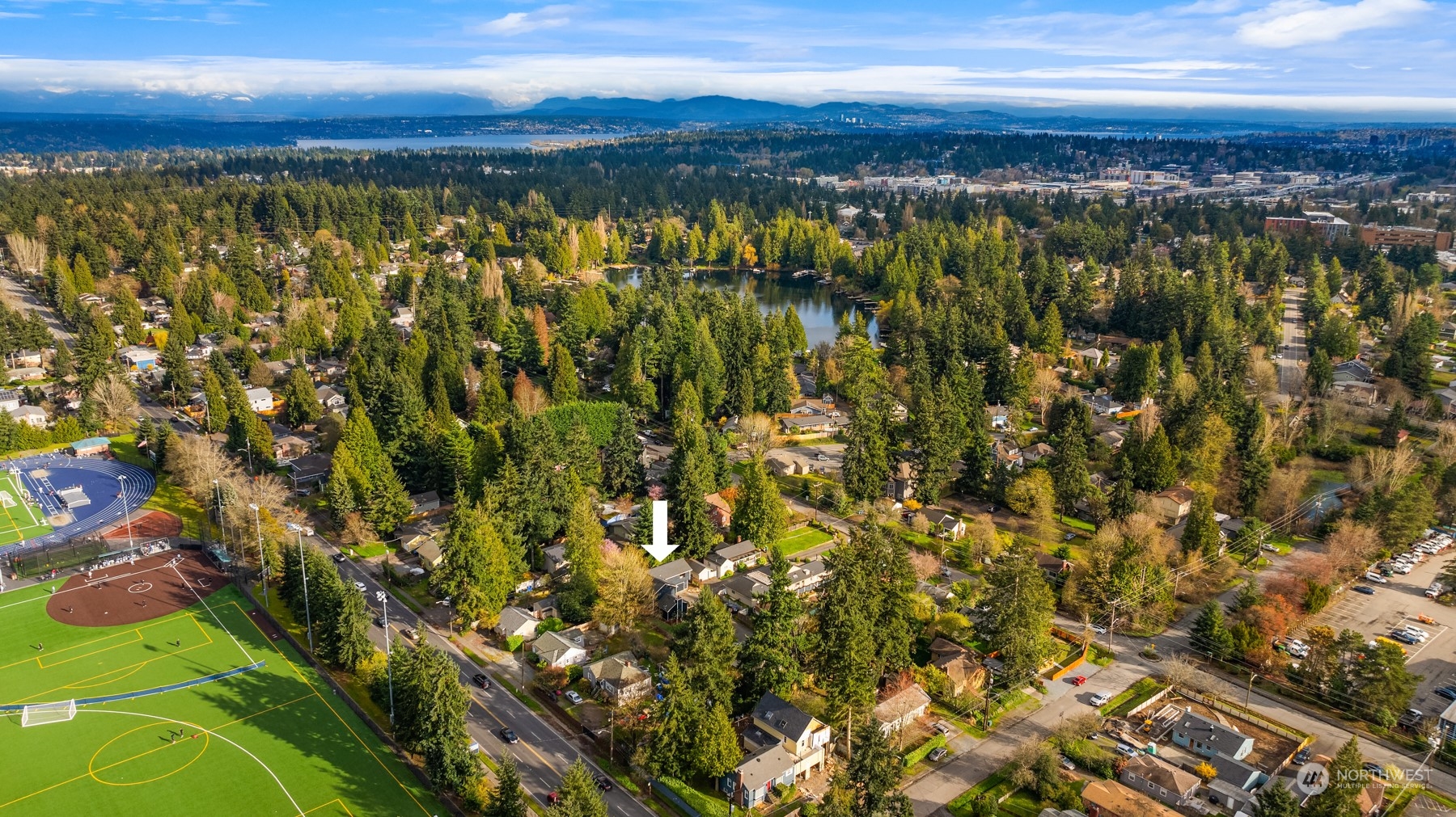 Aerial view of the leafy neighborhood, with an arrow marking the home near sports fields and a lake.