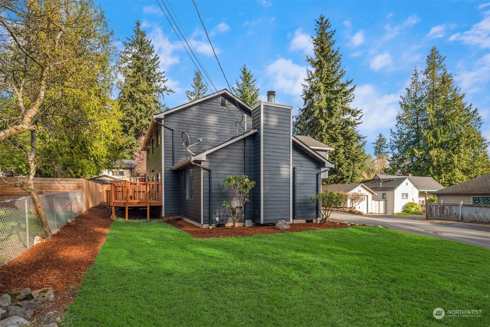 Dark gray two-story house with a tall chimney, wooden deck, and broad green lawn.