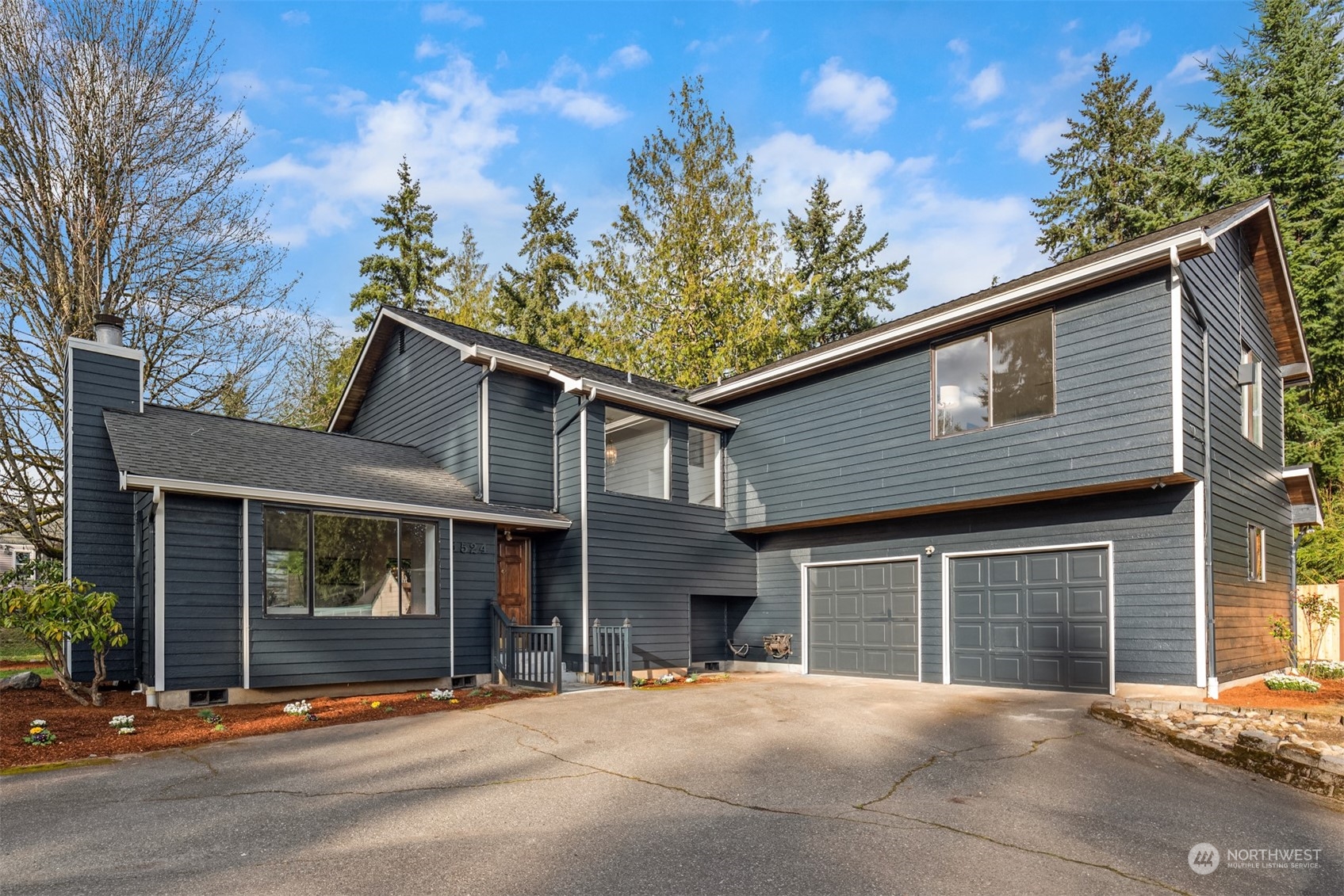 Modern dark blue two-story home with a two-car garage and mature trees.