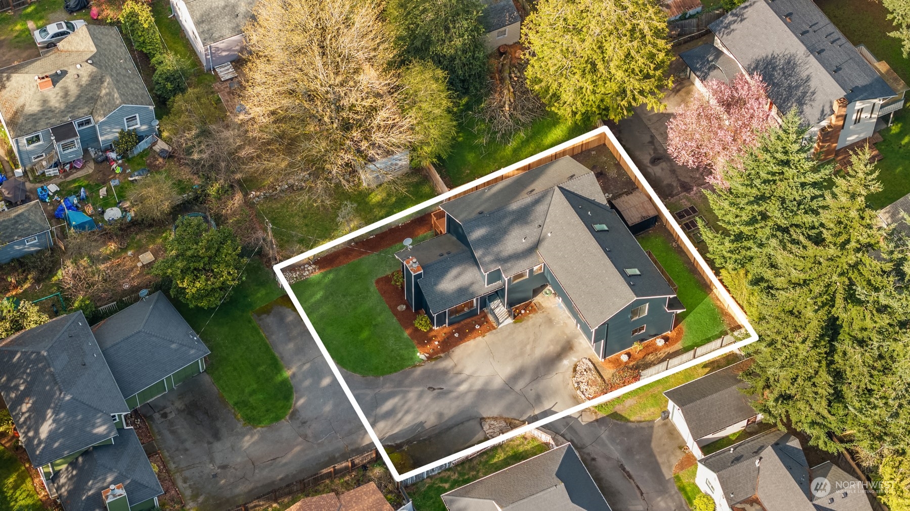 Aerial view of a dark-sided home and its lot, outlined in white, with a broad driveway and lawn.