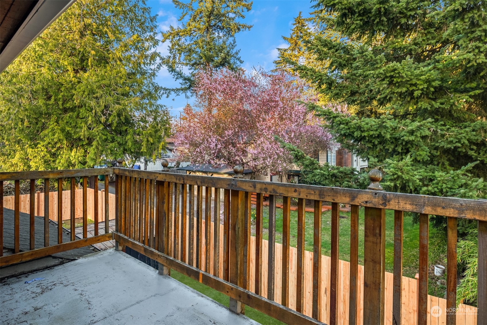 Raised deck overlooking a fenced lawn and mature trees, including a flowering pink tree.