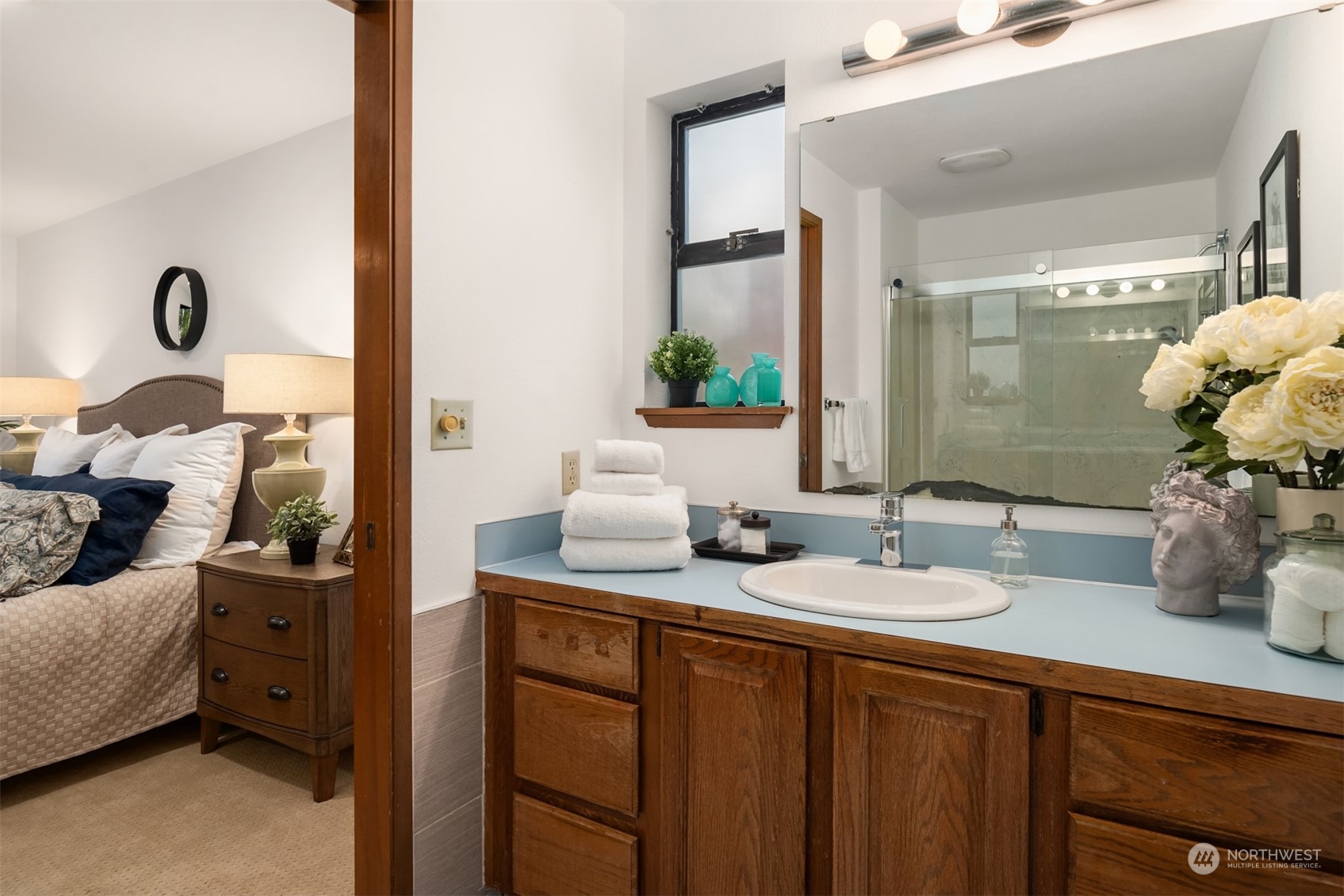 Bathroom with blue countertop, wood vanity, and glass shower; bedroom visible through the doorway.