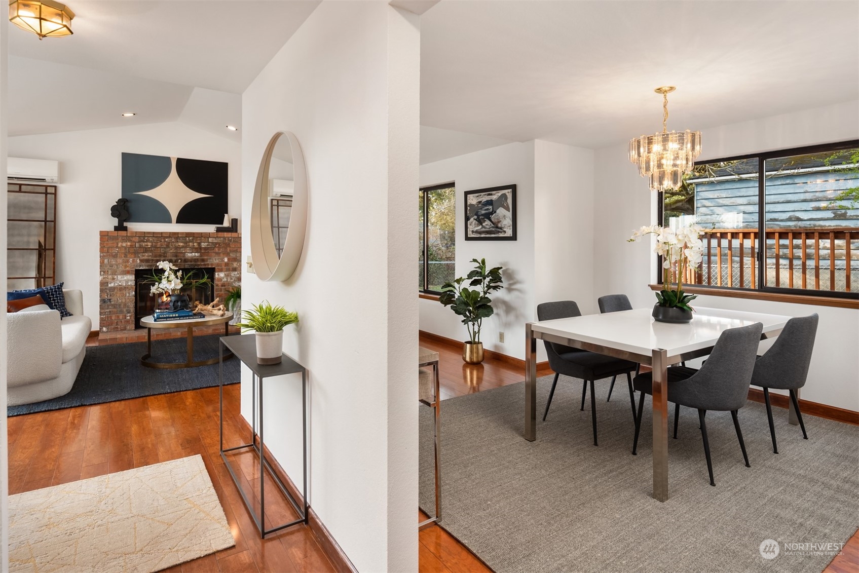 Open-plan living and dining room with a brick fireplace, hardwood floors, and a chandelier above the dining table.