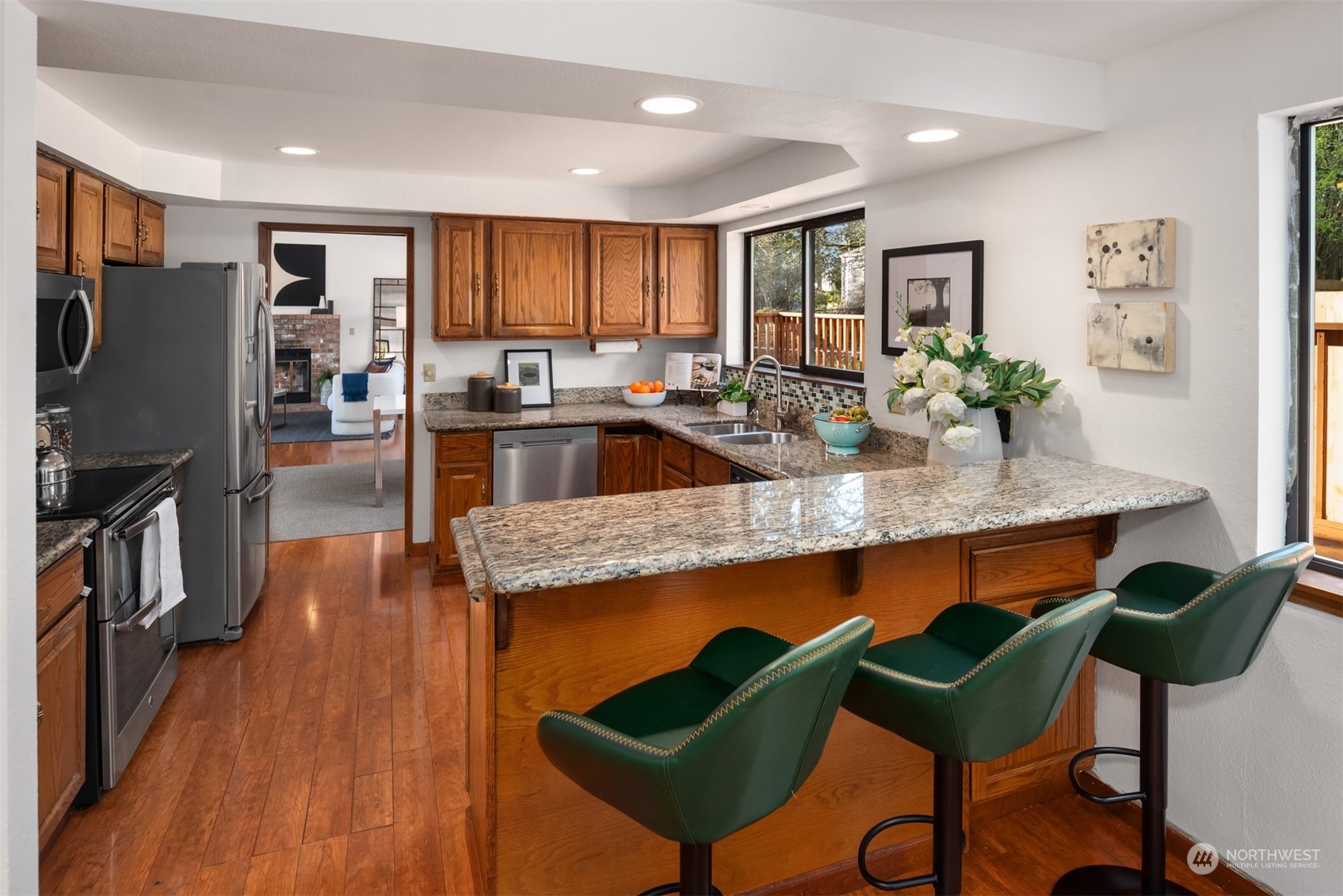 Kitchen with granite breakfast bar, dark green stools, wood cabinets, and stainless steel appliances.
