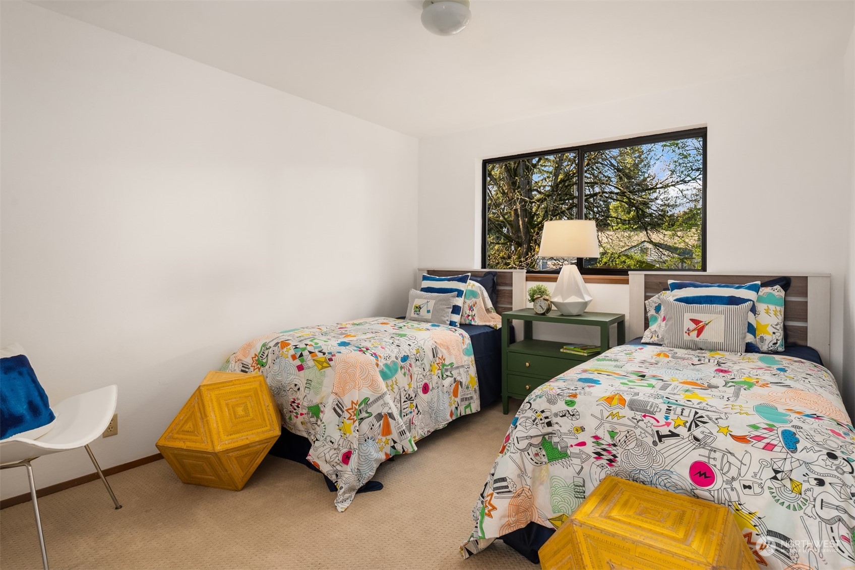 Bedroom with two twin beds, colorful patterned bedding, and a large window overlooking trees.