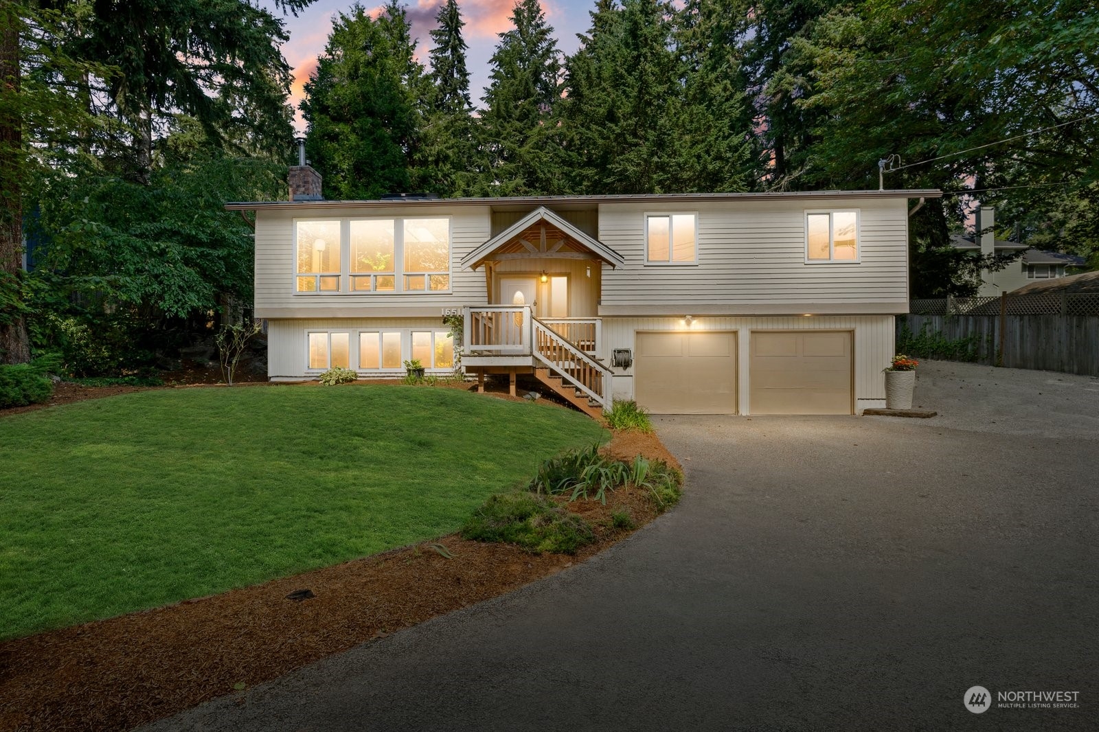 Two-story home with peaked entry, double garage, broad lawn, and evergreens at dusk.