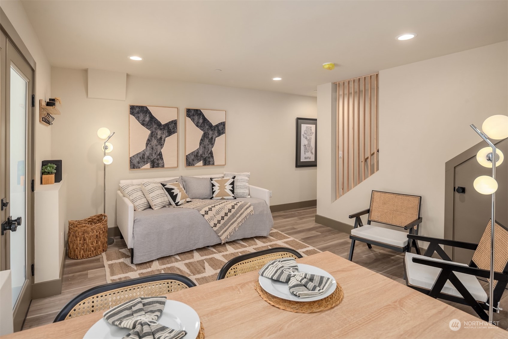 Staged living and dining area with a gray sofa, patterned rug, and wood-slat staircase.