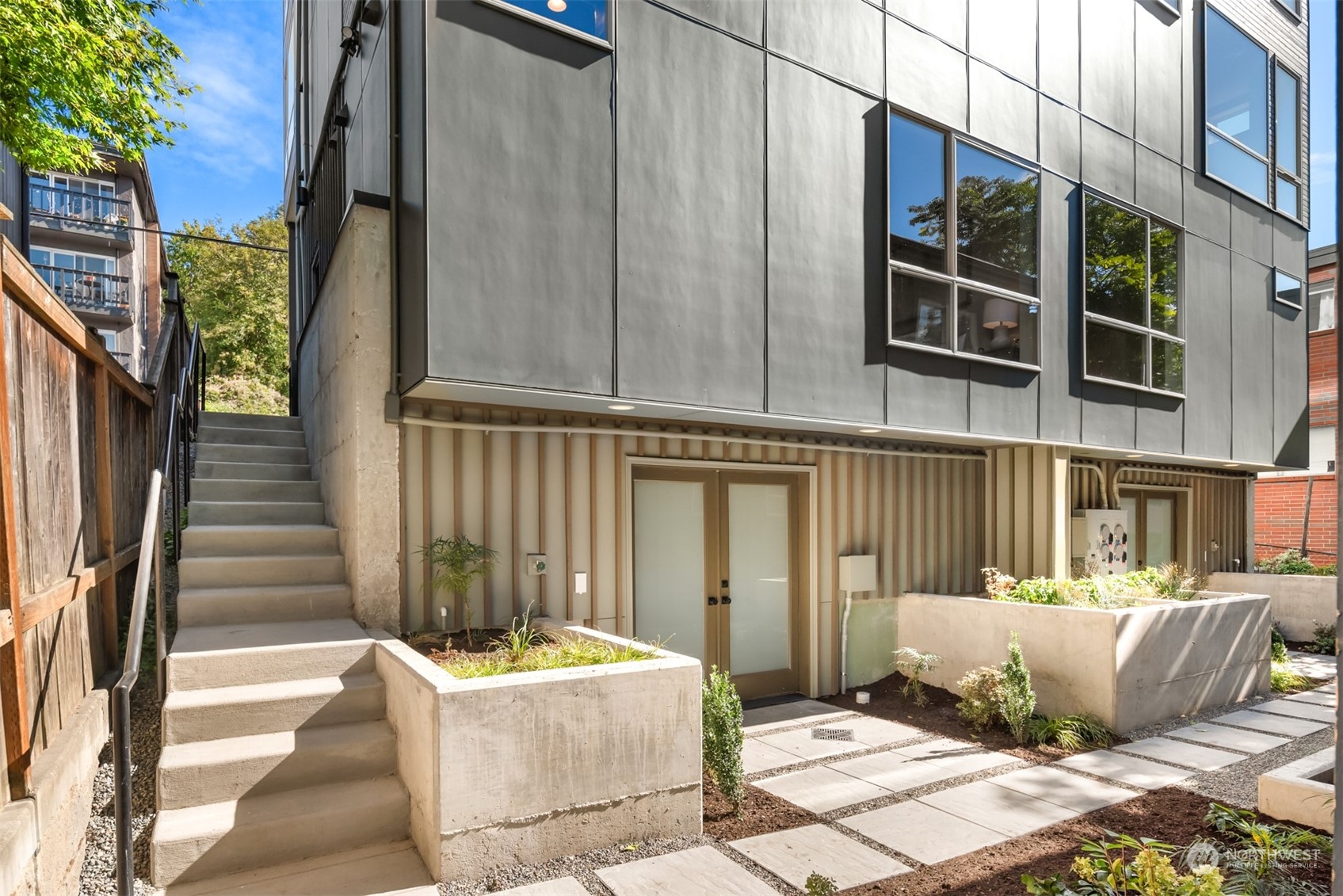 Modern gray residence with a private entrance, concrete stairs, and raised courtyard planters.