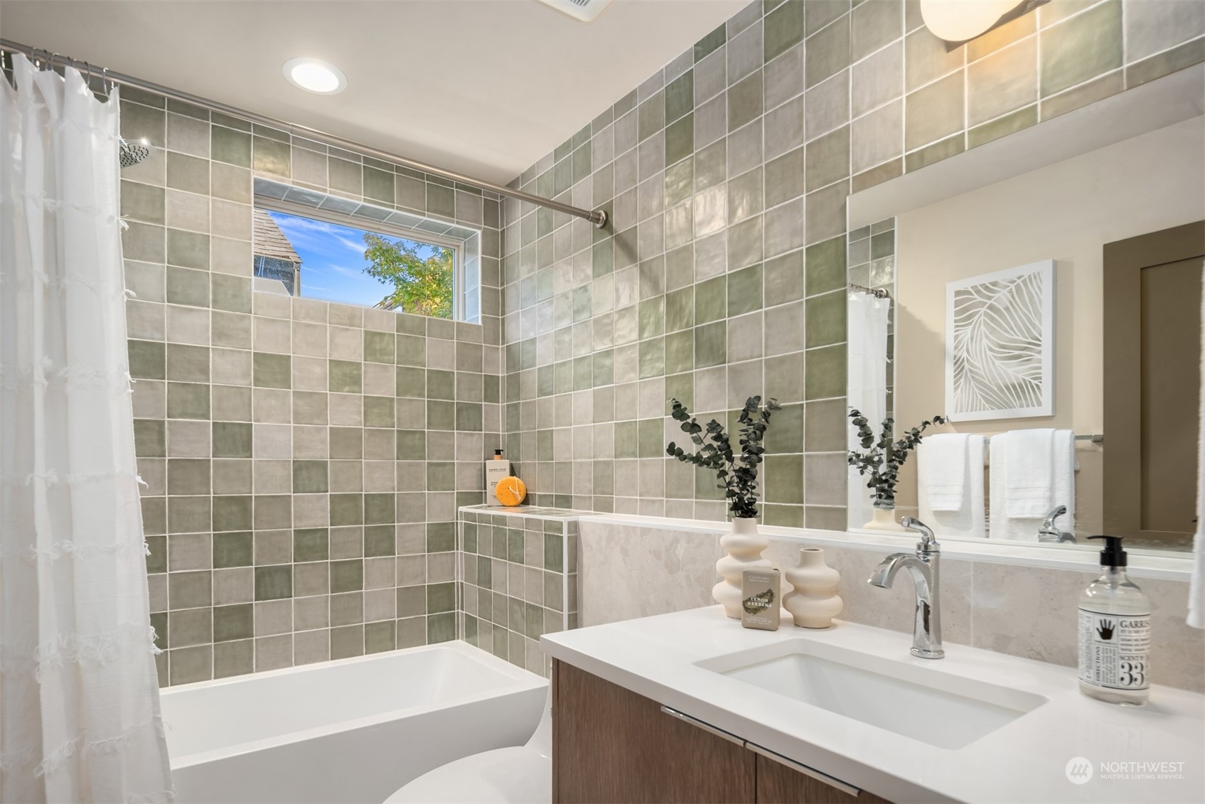 Bathroom with green and gray tiled tub surround, a window, and a wood vanity.