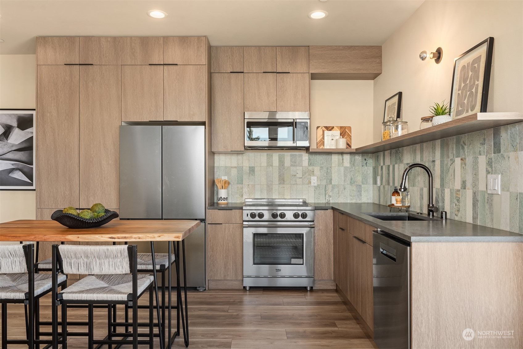 Modern kitchen with light wood cabinetry, stainless steel appliances, and a green-and-cream tiled backsplash.