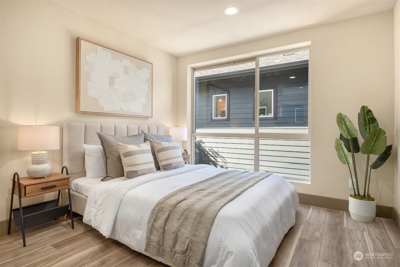 Staged bedroom with a large bed, neutral bedding, and a wide window.