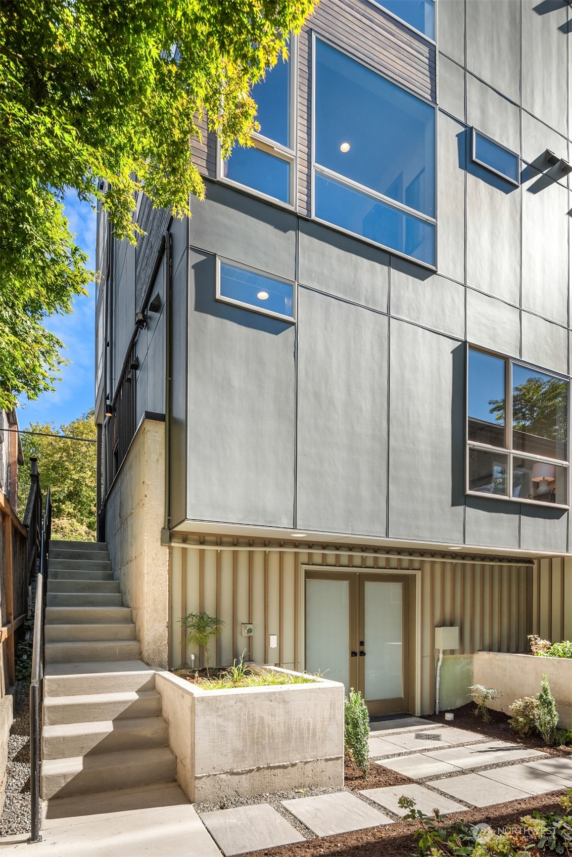 Modern gray residence with large windows, concrete entry steps, and a landscaped courtyard.