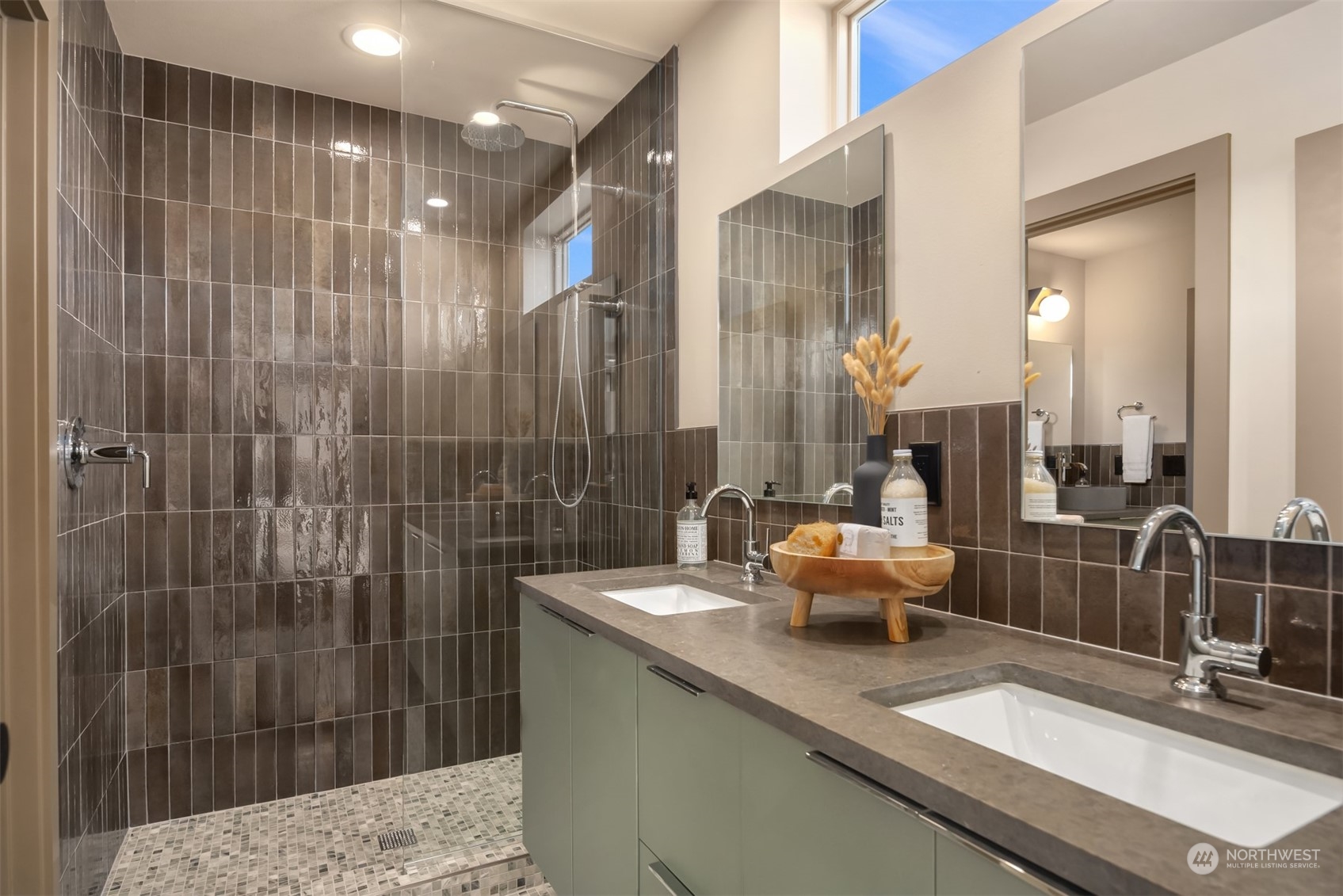 Bathroom with a dark tiled walk-in shower and double vanity beneath large mirrors.