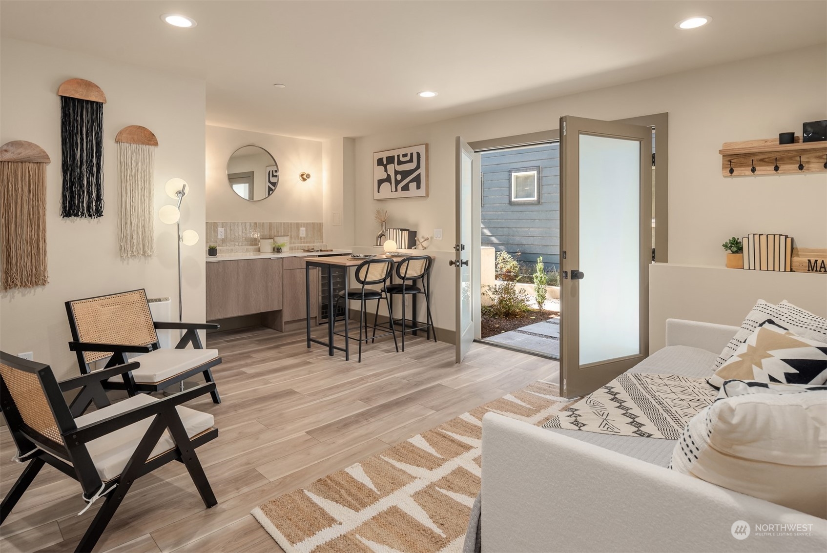 Staged living room with a compact kitchen, breakfast bar, and open door to a planted patio.