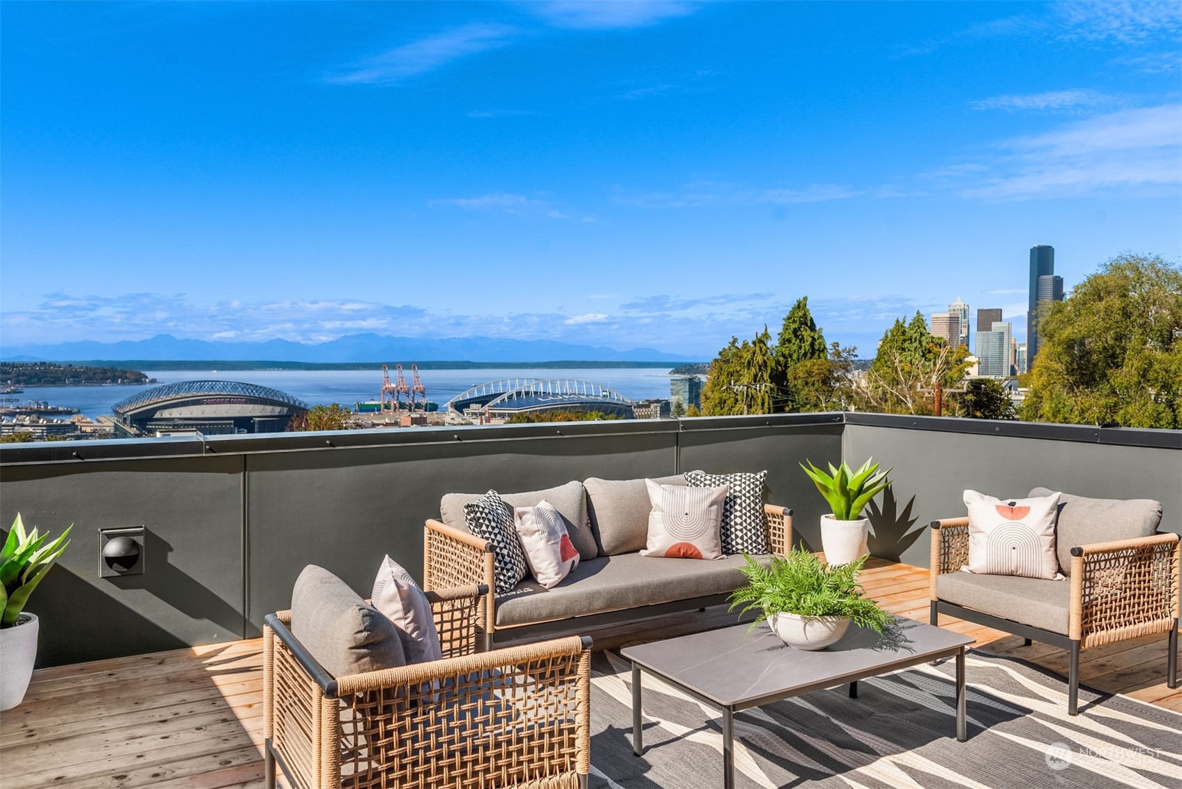 Rooftop deck with wicker seating overlooking Elliott Bay, Seattle’s stadiums, and downtown skyline.