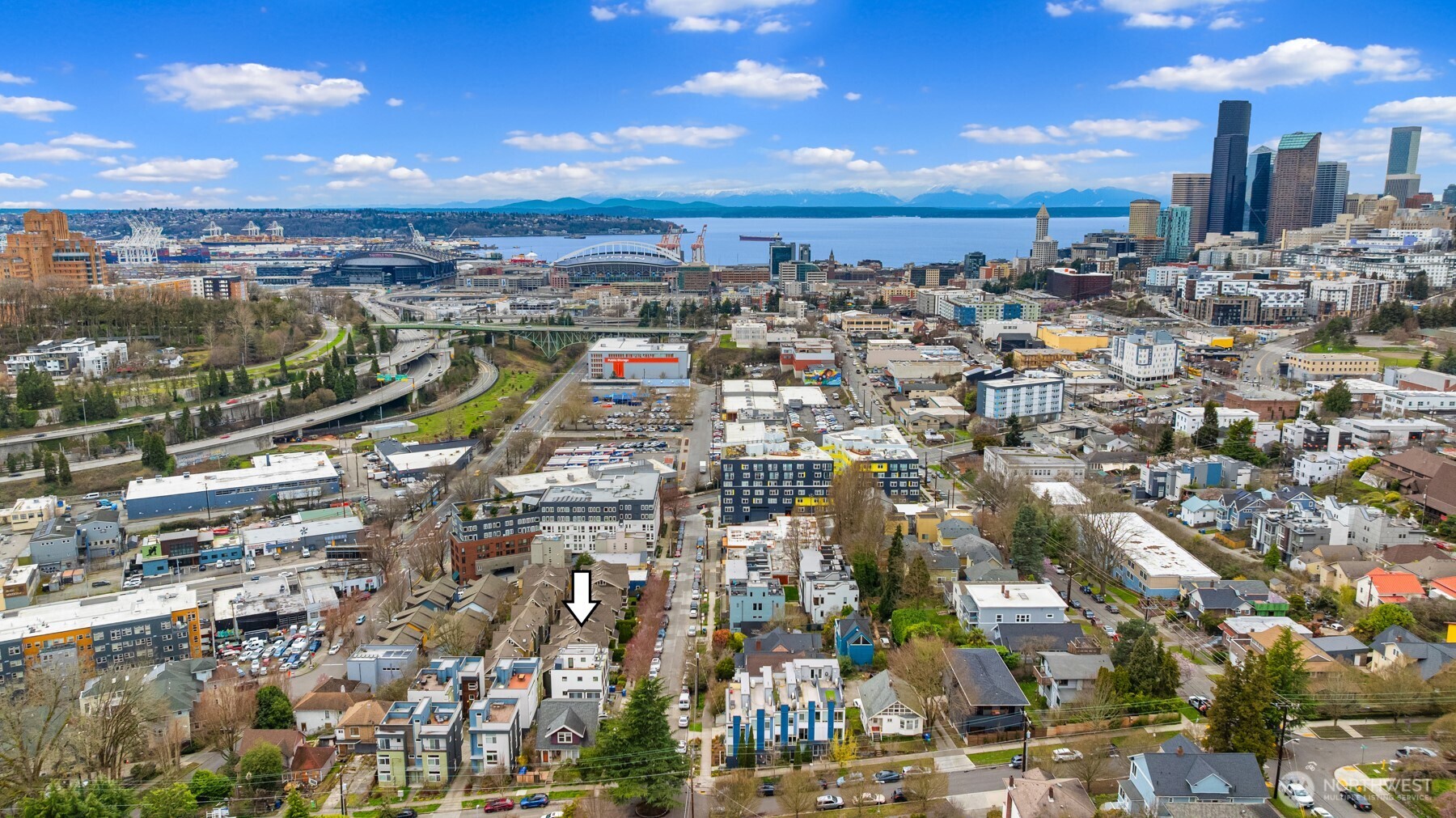 Aerial view of the arrow-marked property, with Seattle’s skyline, bay, and distant mountains.